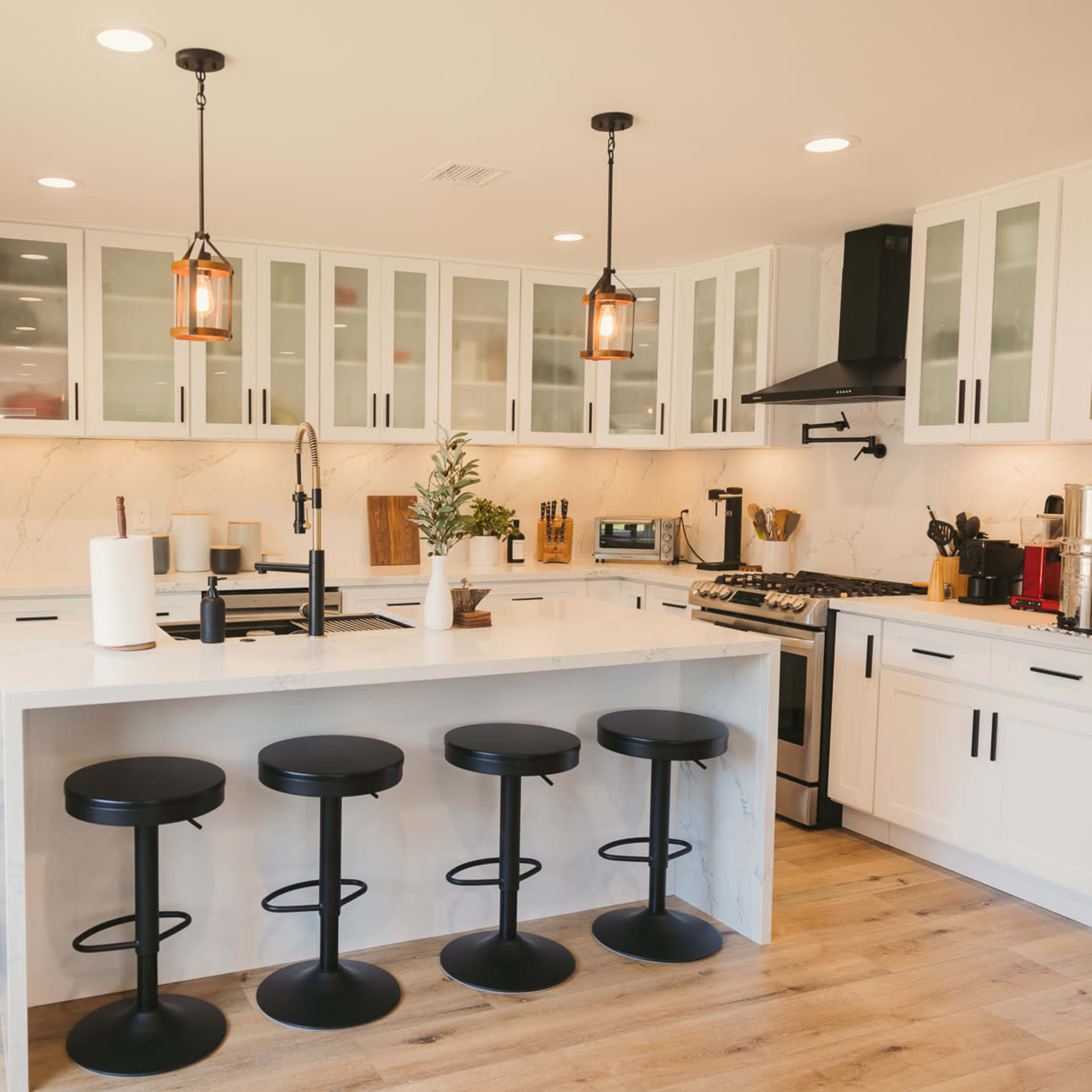 A modern kitchen features a central island with four black bar stools, white cabinetry, and stainless steel appliances.