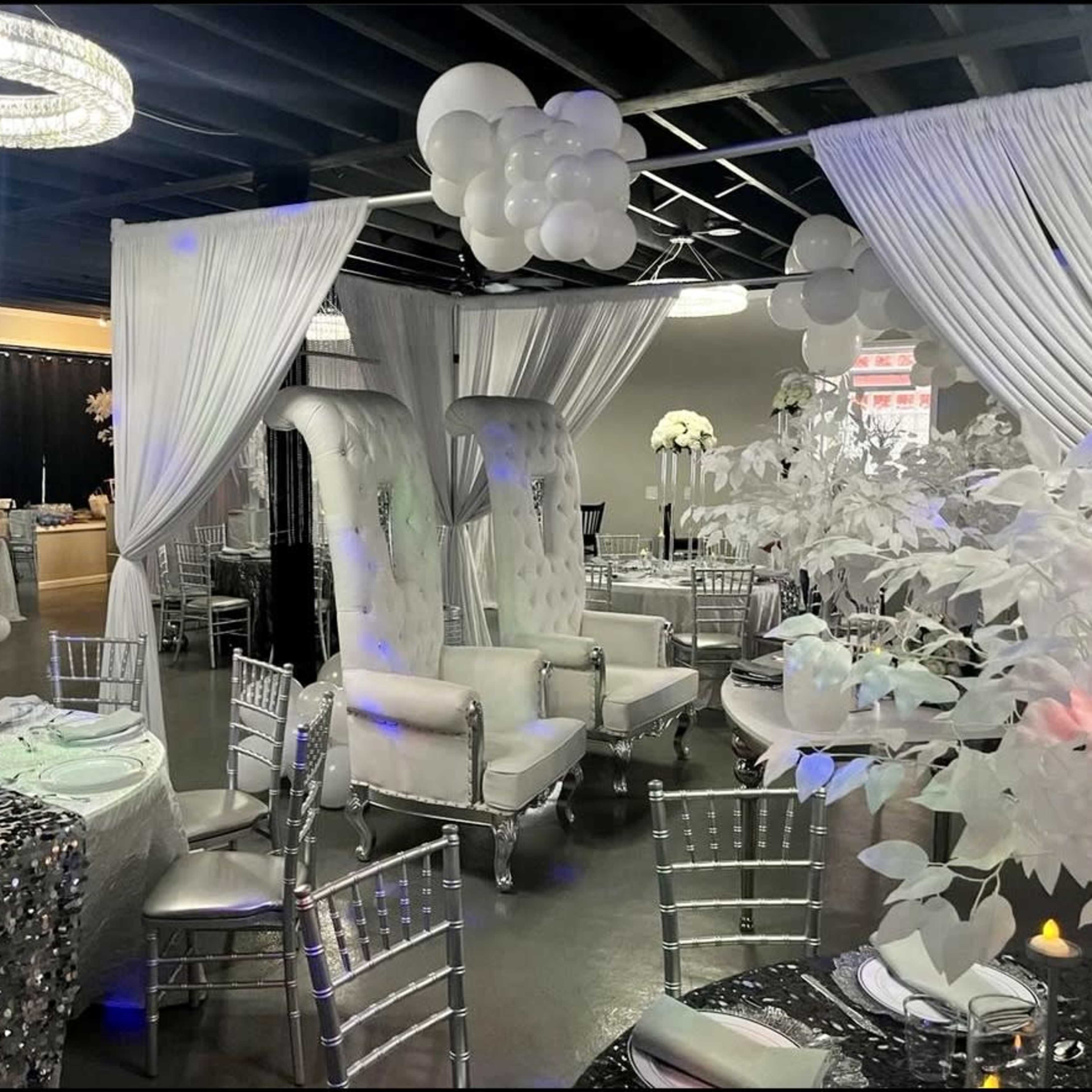 A decorated event space with elegantly set round tables, white drapery, and plush seating arranged for a formal gathering.