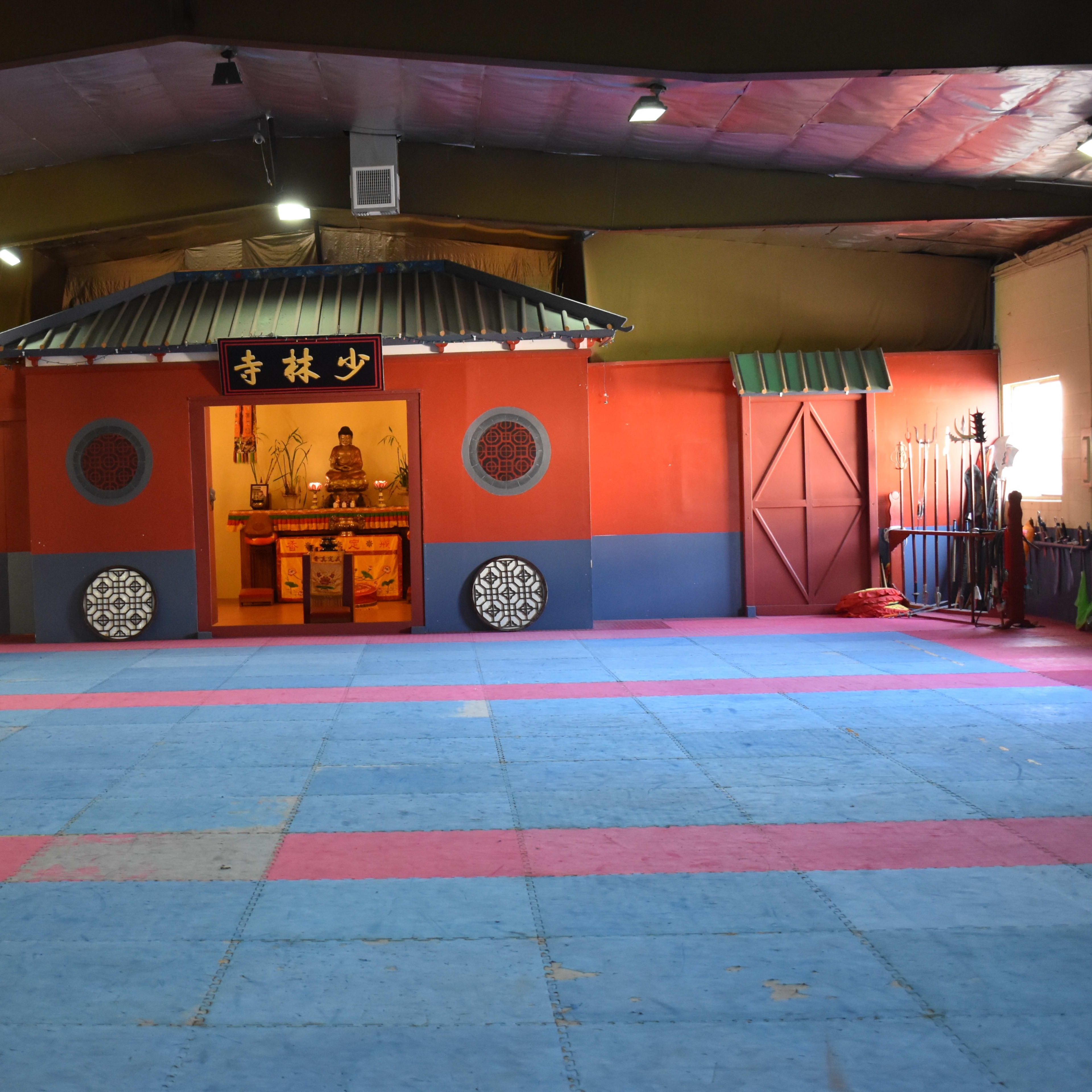 A martial arts training hall with a brightly colored entrance and various weapons displayed around the perimeter.