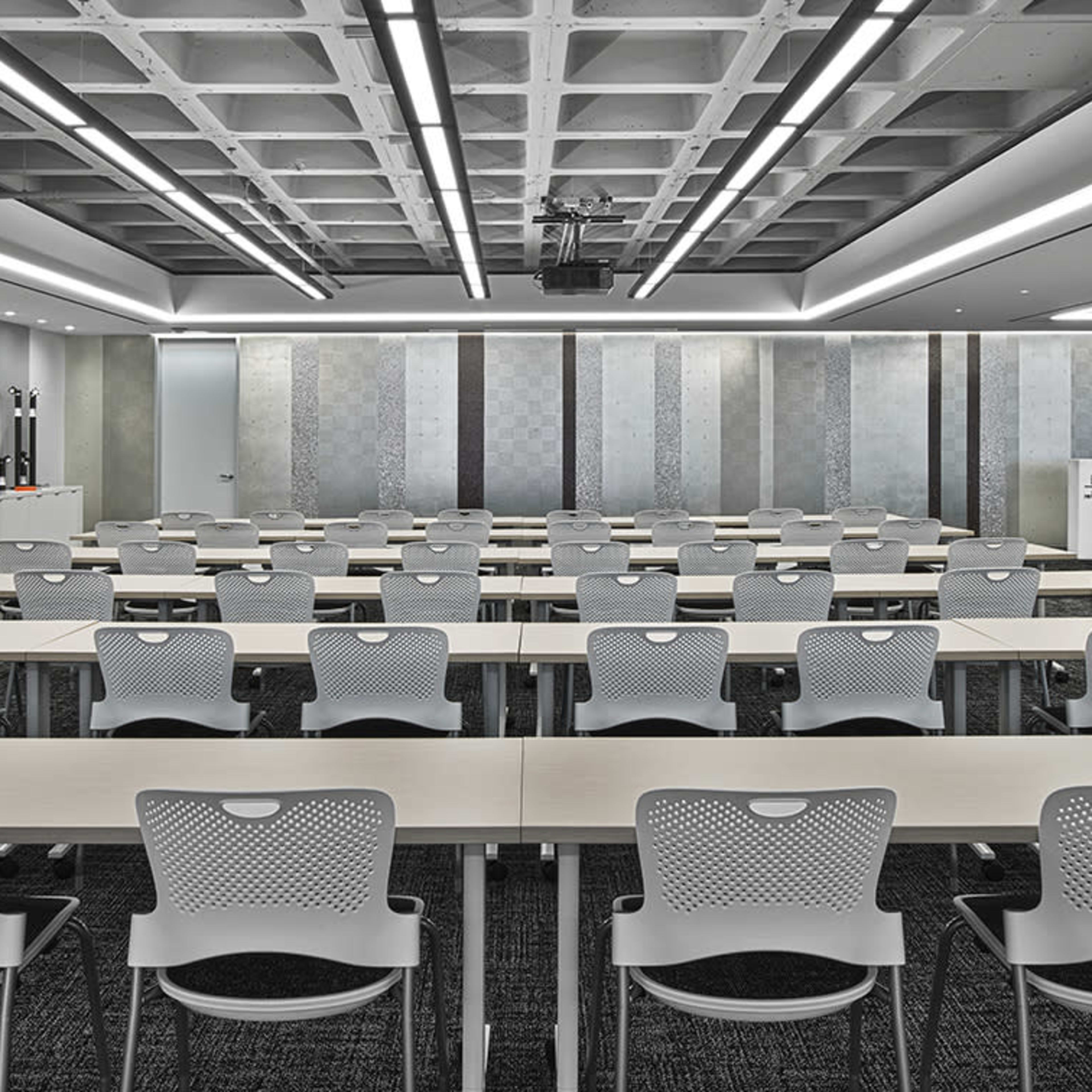 A modern conference room arranged with multiple rows of tables and chairs, designed for meetings or presentations.