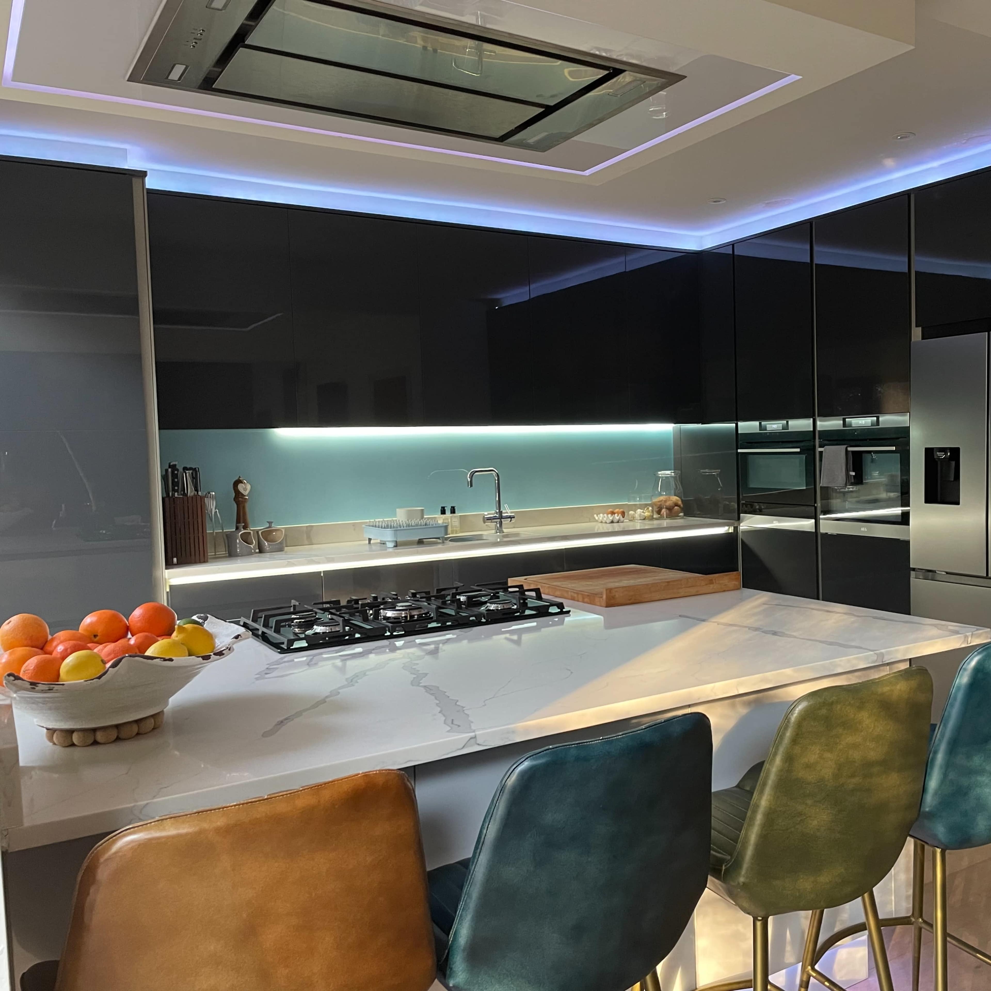 A modern kitchen features a central island with bar stools, sleek black cabinetry, and a large gas cooktop.