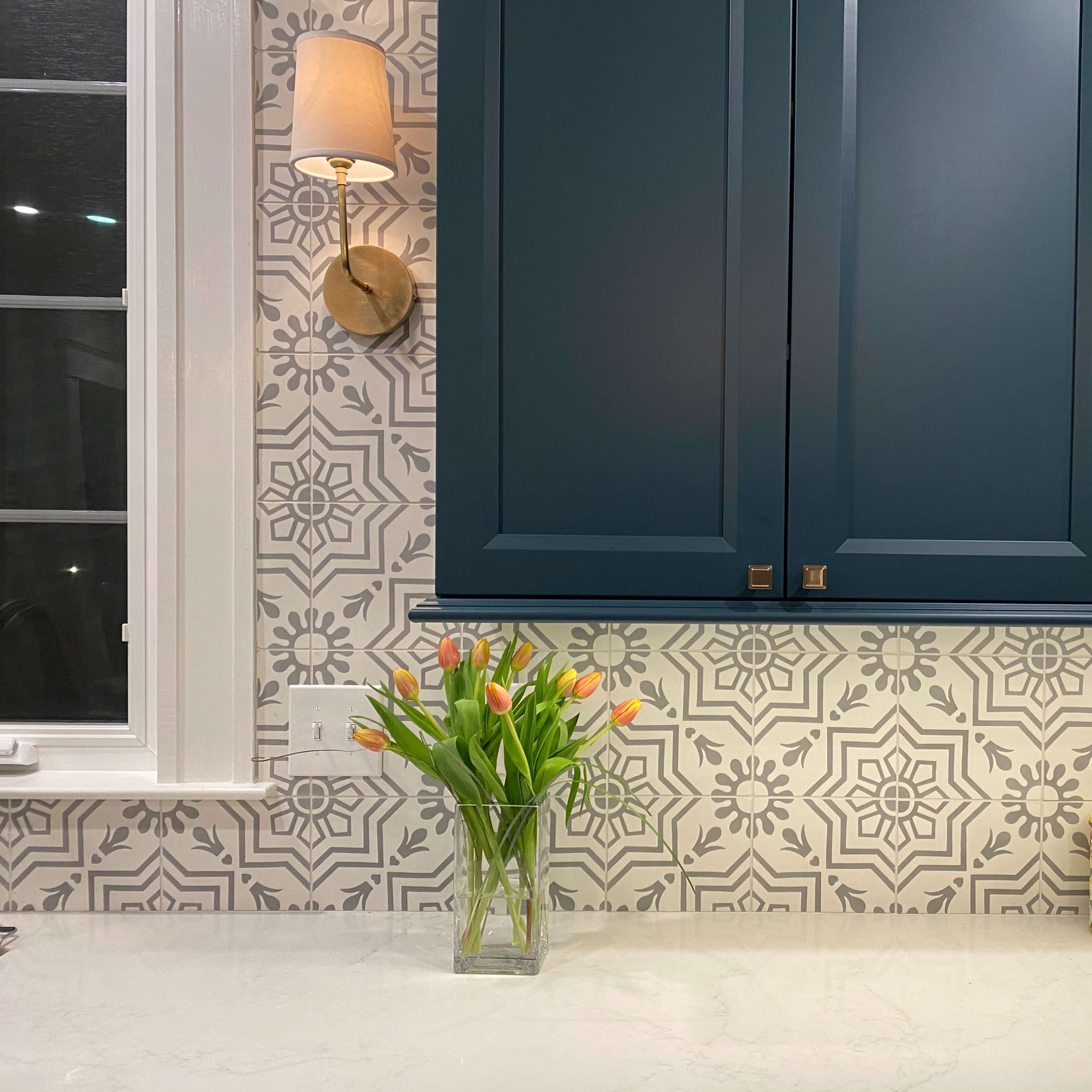 A kitchen countertop with a vase of tulips, decorative canisters, and patterned backsplash behind dark blue cabinets.