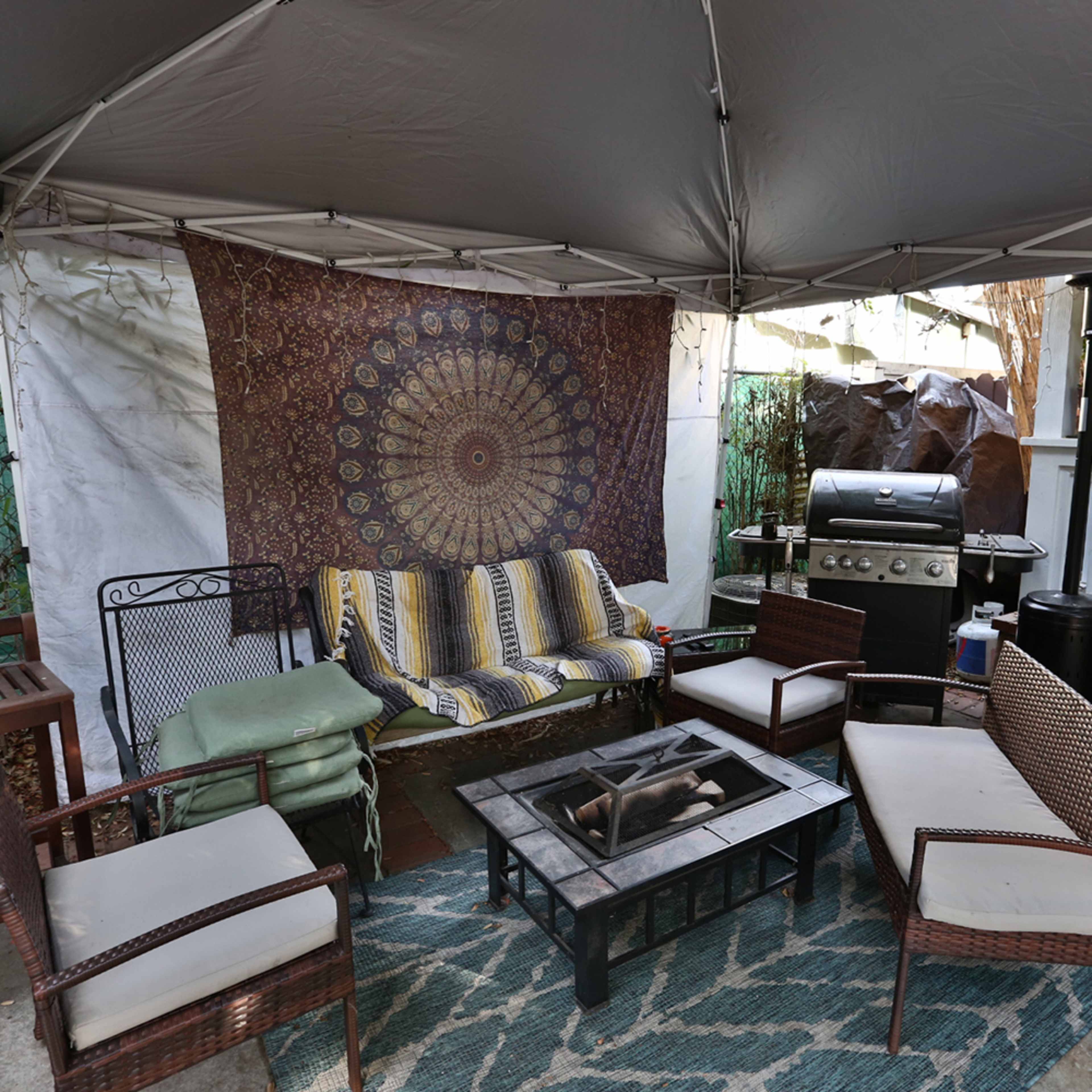 A covered outdoor seating area features a seating arrangement with chairs and couches, a grill, and a fire pit on a patterned rug.