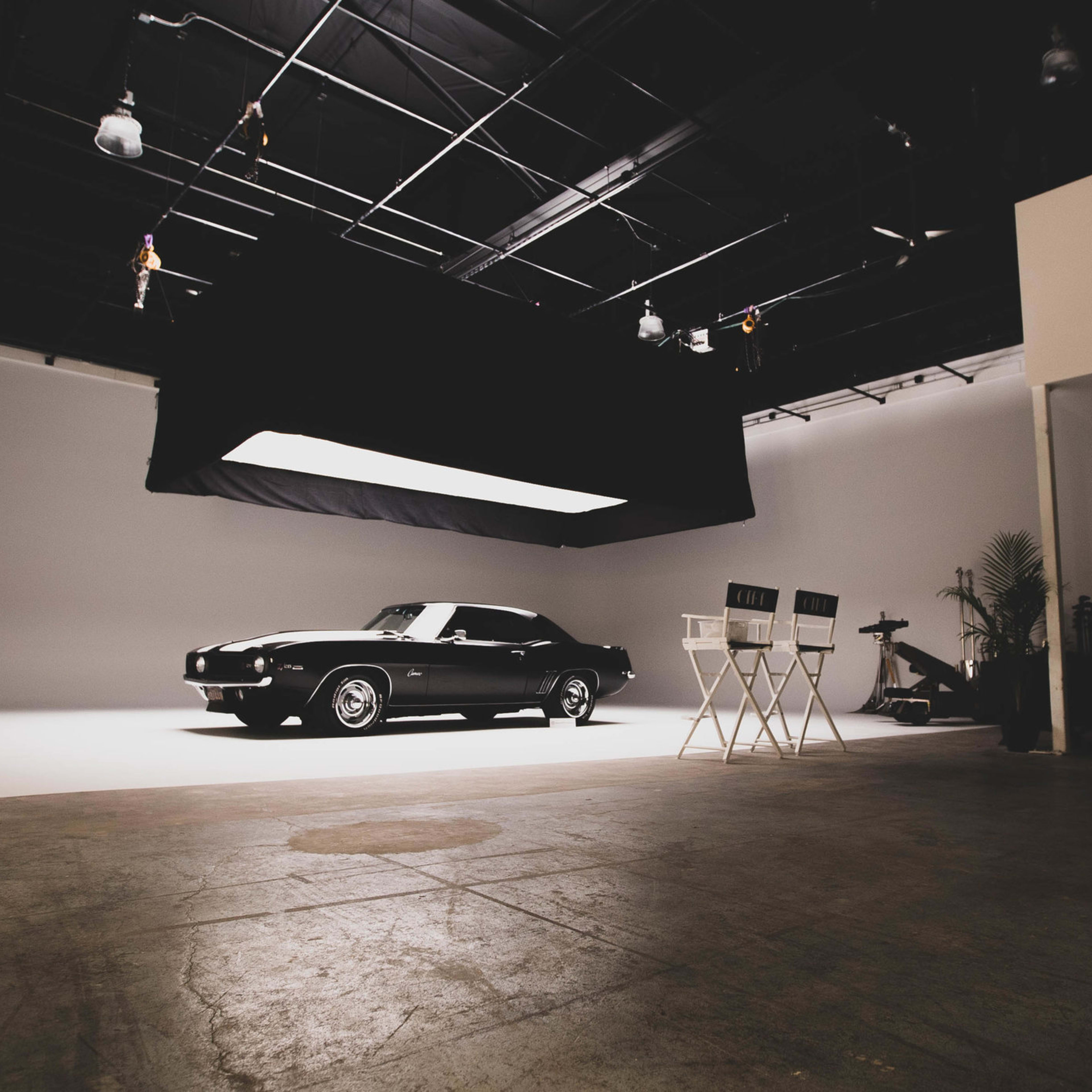 A classic black car is parked in a spacious, well-lit photography studio with minimalistic decor.