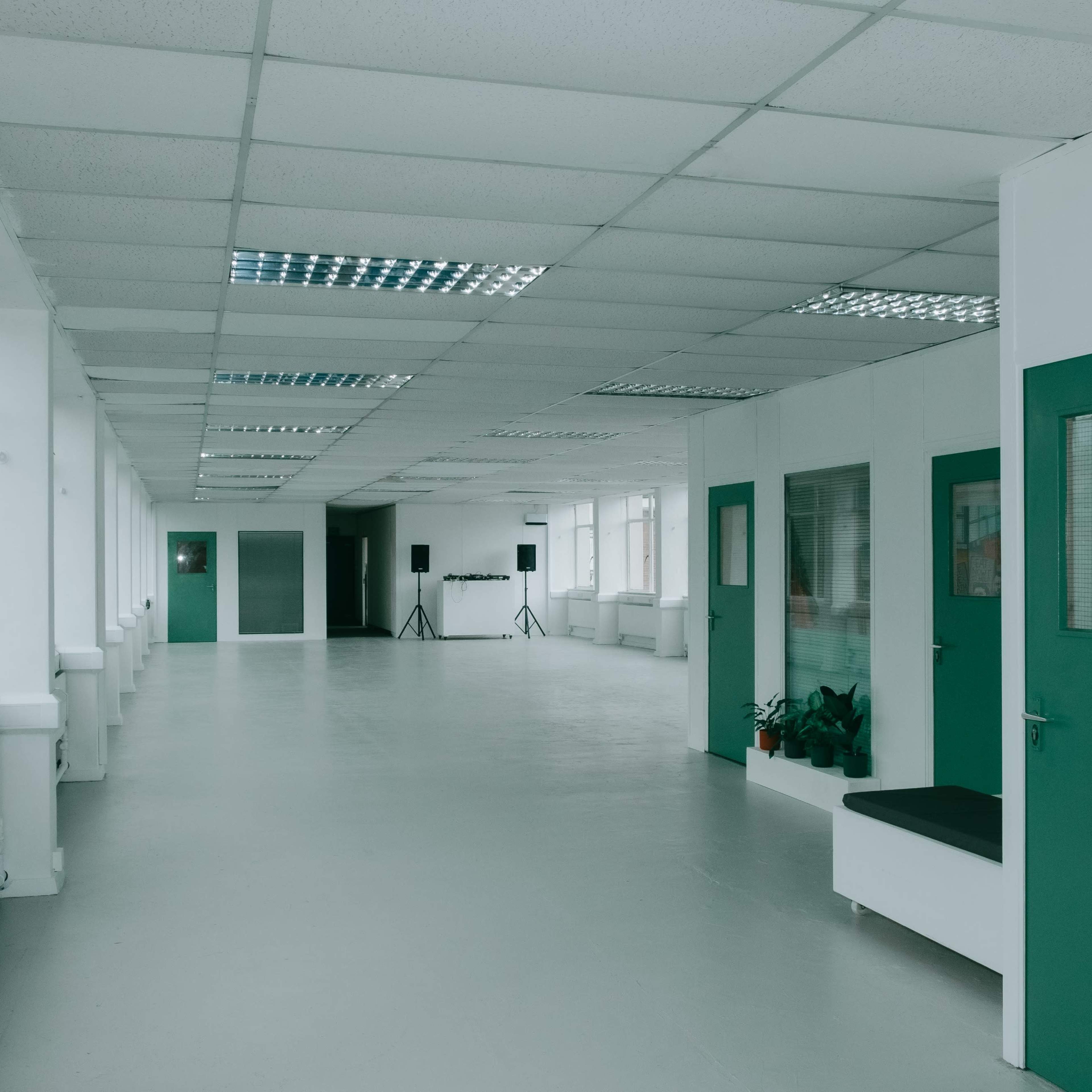 A long, empty hallway in a brightly lit building features green doors and a minimalist design.