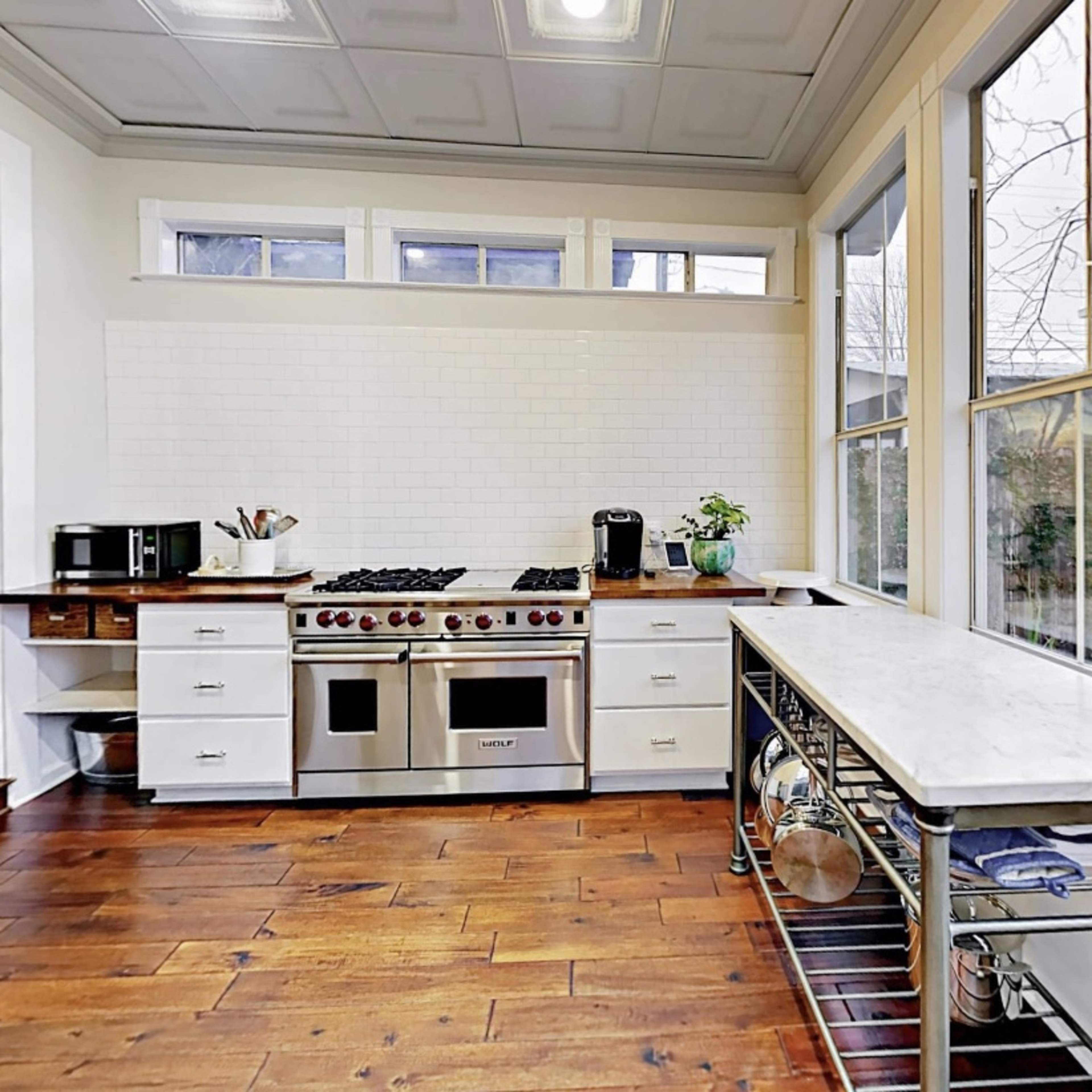 A modern kitchen features a marble countertop, gas stove, and large windows that provide natural light.