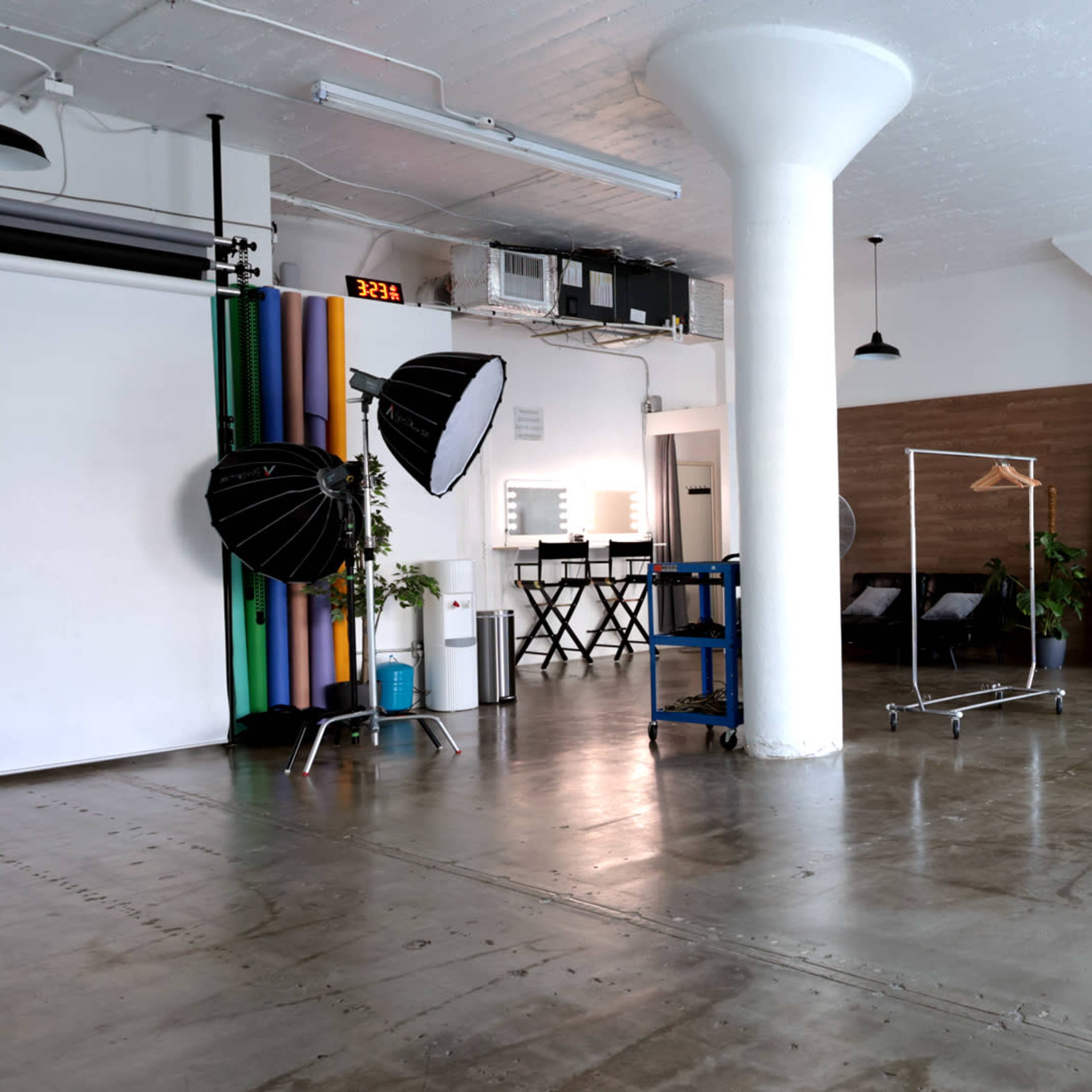 A spacious studio with a photography backdrop, lighting equipment, a mirror, and a clothing rack.
