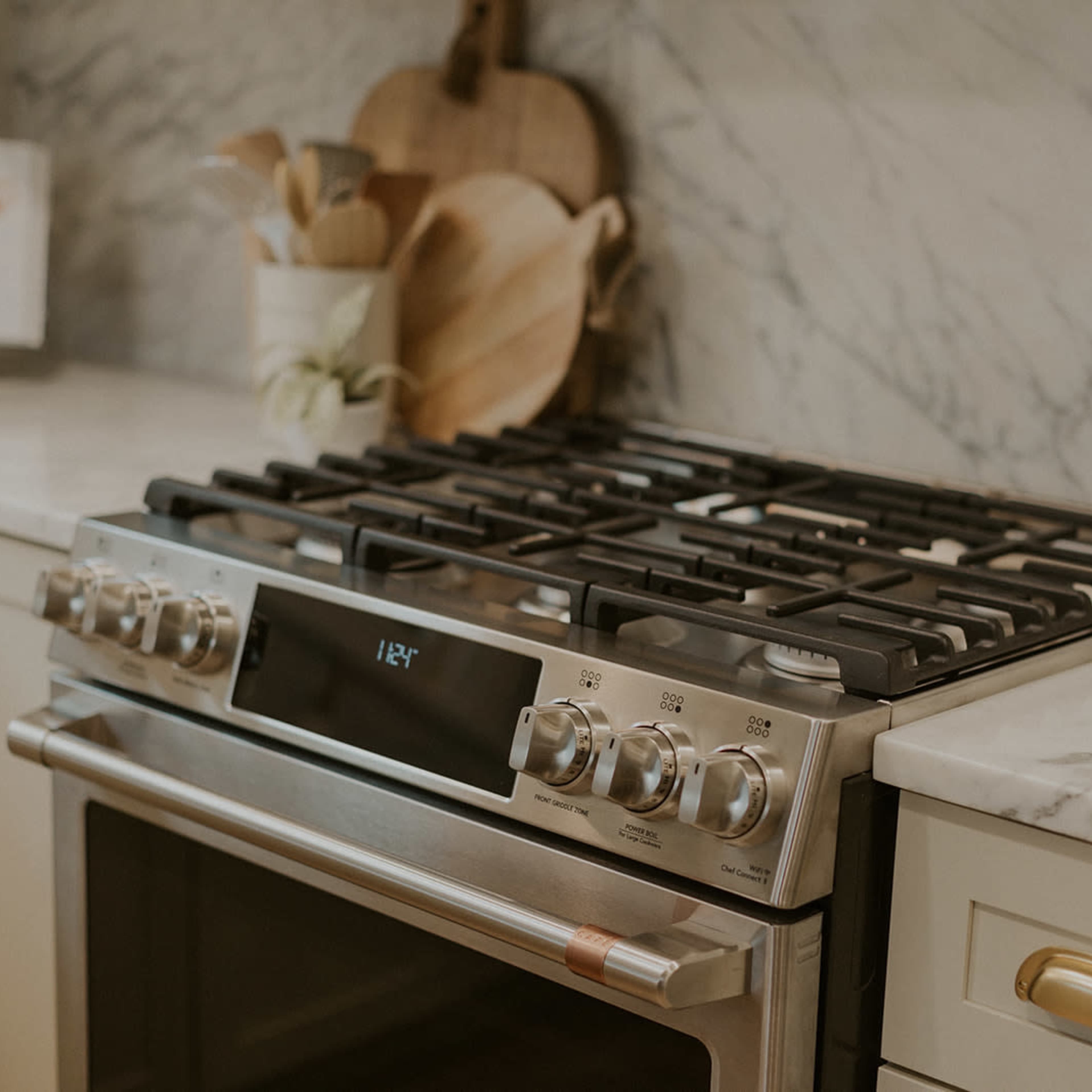 A stainless steel gas range on a marble countertop, accompanied by wooden cutting boards and kitchen utensils.