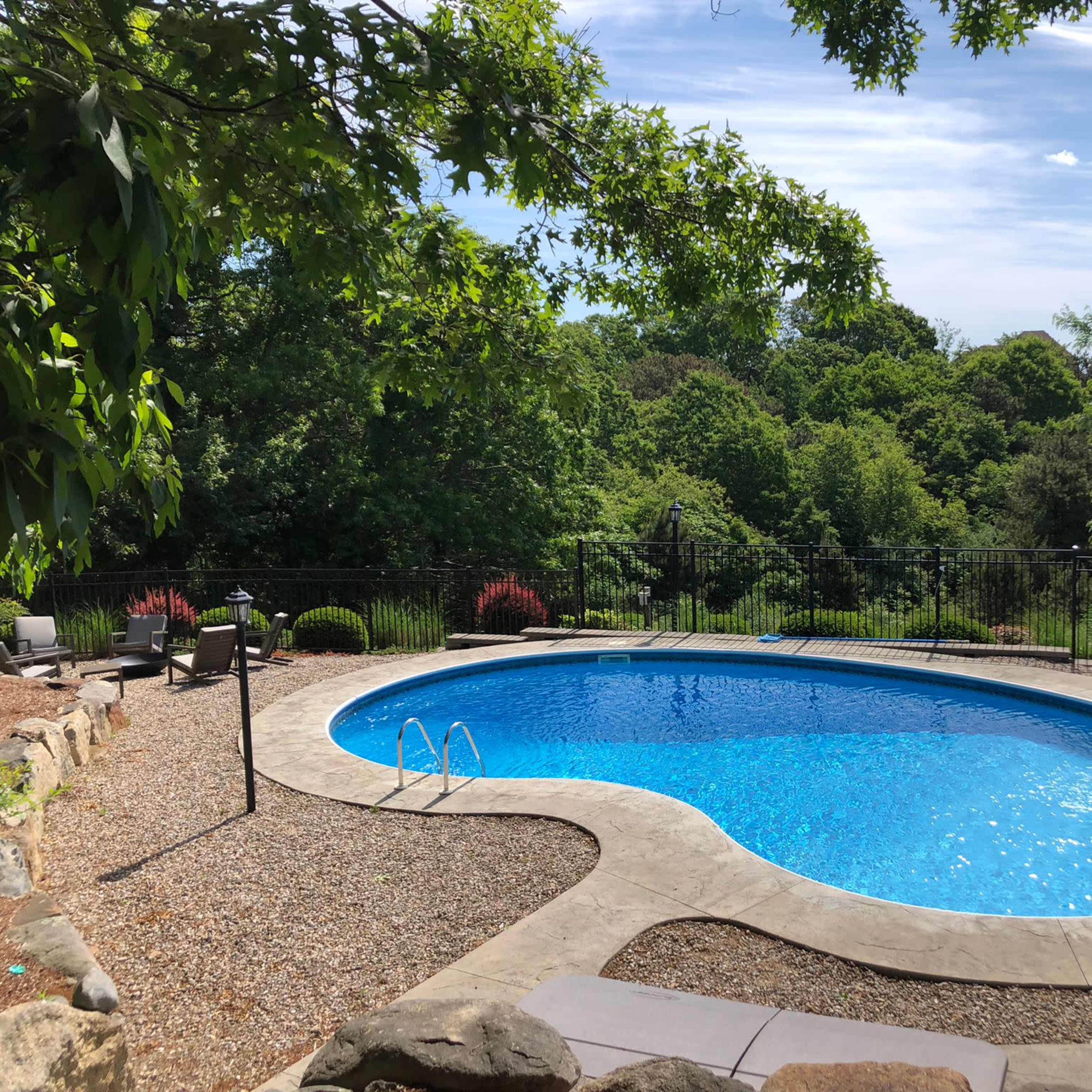 A rectangular swimming pool surrounded by a gravel patio and landscaped greenery.