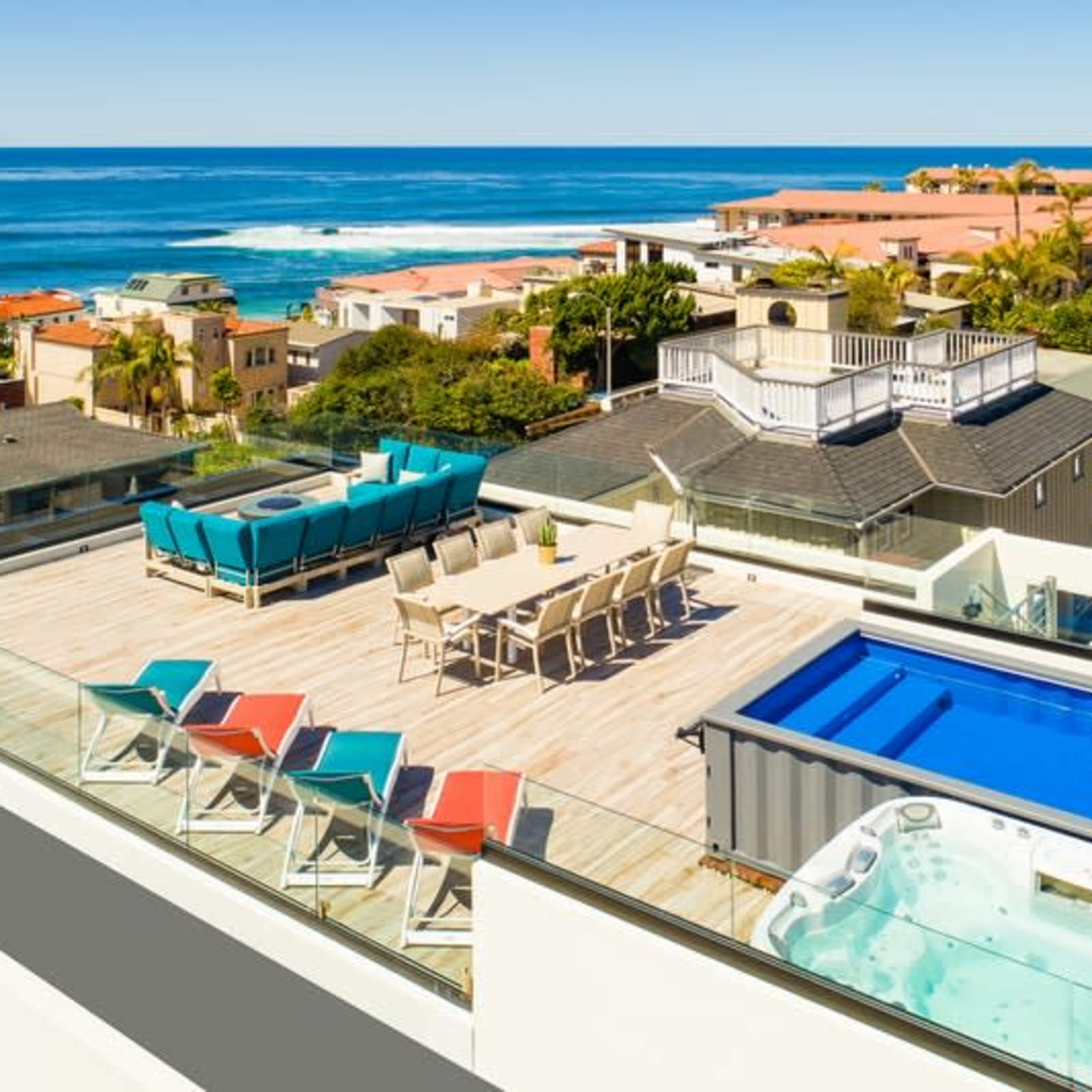 The rooftop features a large dining area, a swimming pool, a hot tub, and several lounge chairs overlooking the ocean.