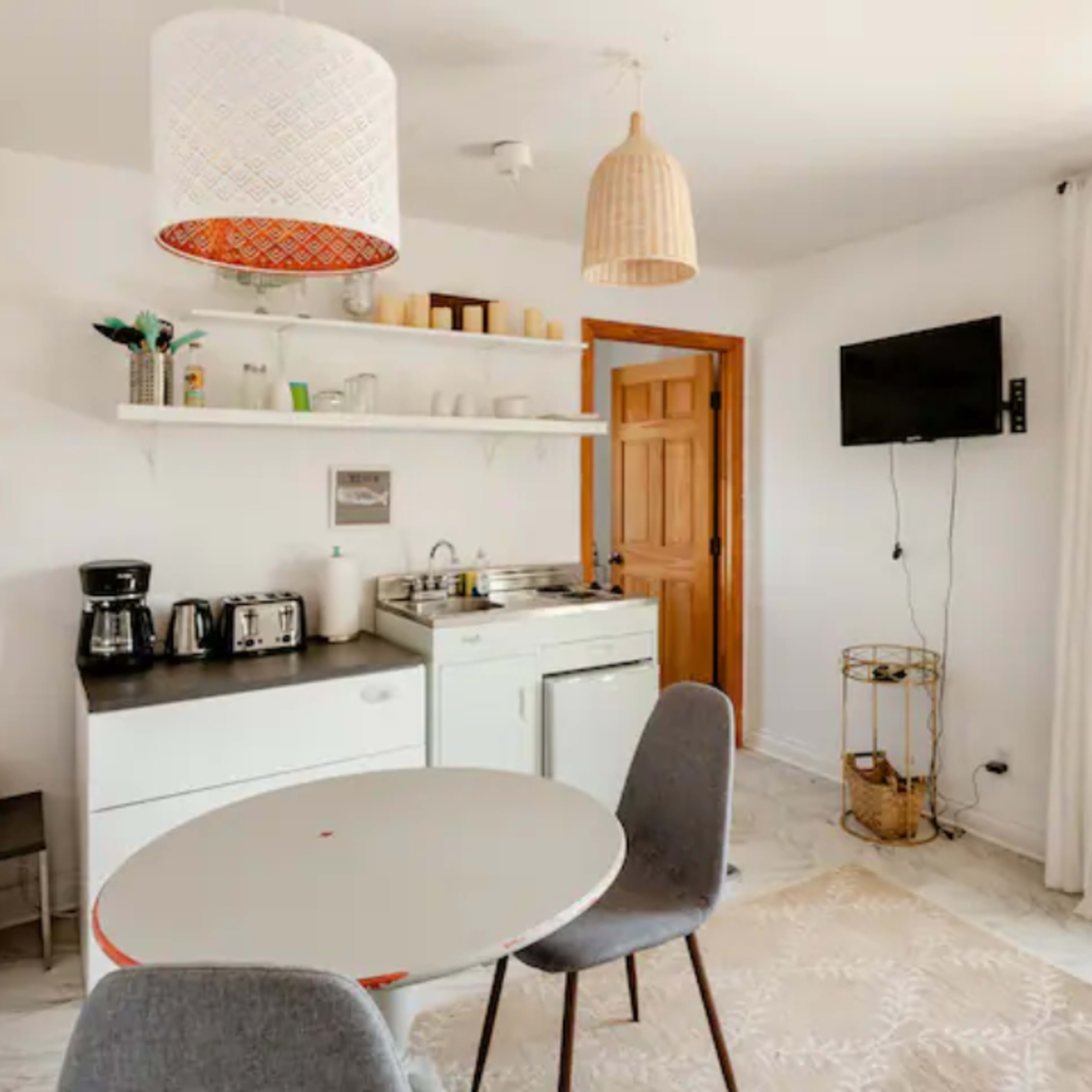 A compact kitchen and dining area with a round table, two chairs, and various kitchen appliances against a light-colored wall.