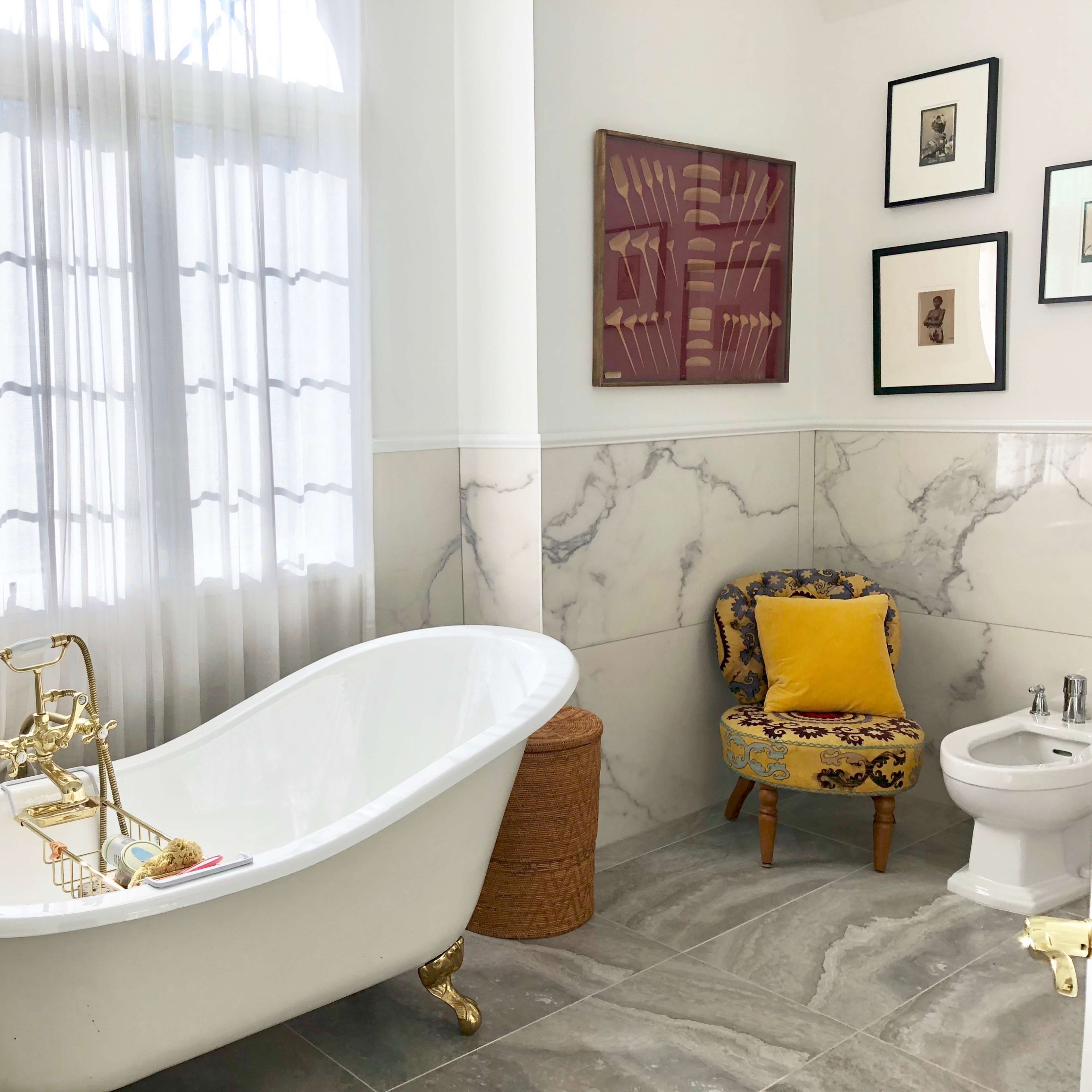 A bathroom featuring a freestanding white bathtub, a small patterned chair, and elegant decor on the walls.