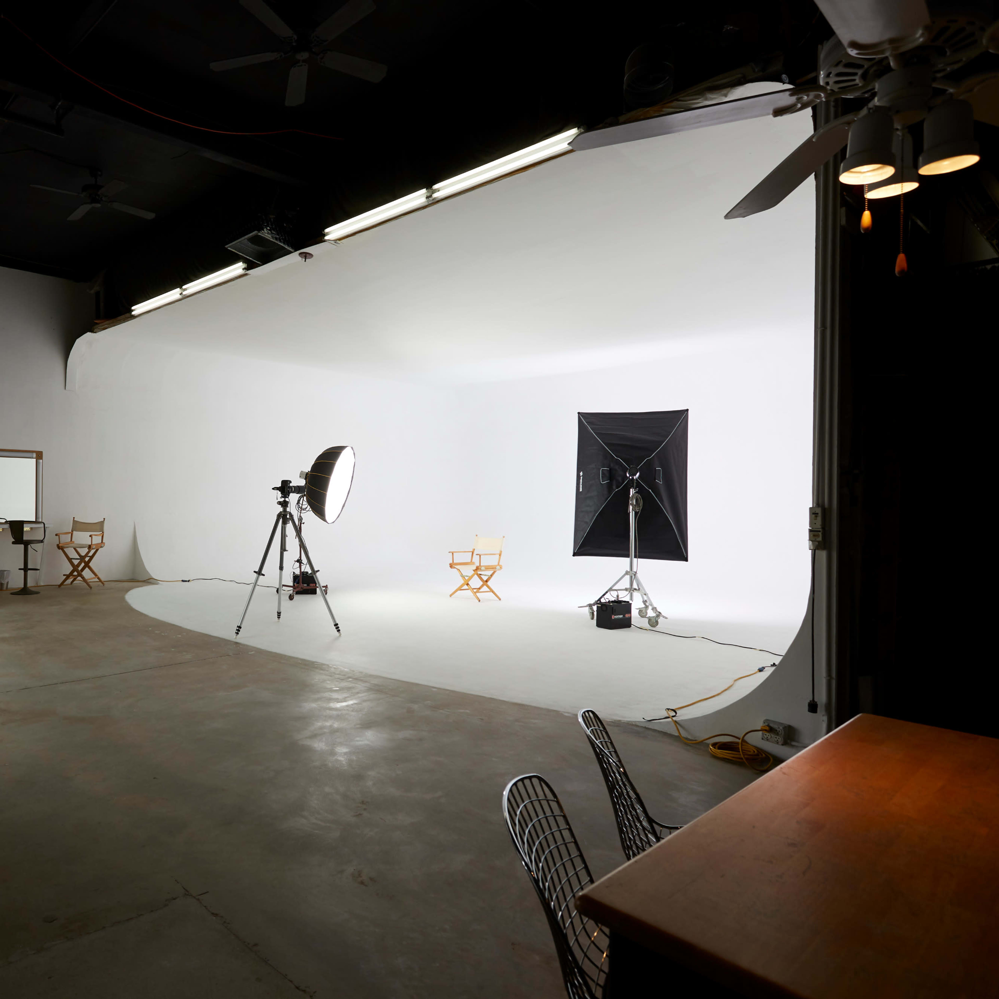 A photo studio with a white backdrop, cameras on tripods, and two director's chairs set up for a shoot.