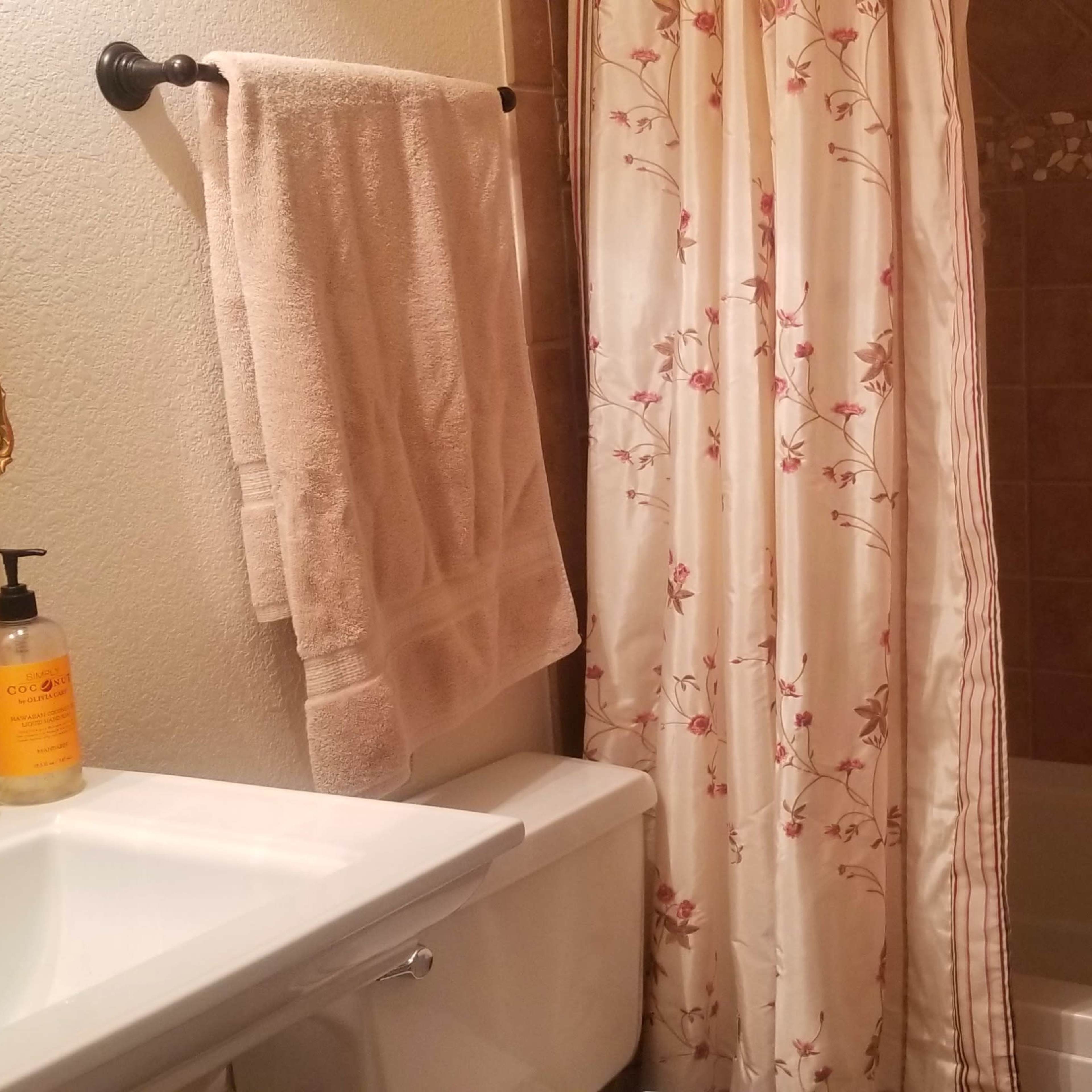 A bathroom featuring a bathtub with a shower curtain, a sink with a soap dispenser, and a towel hanging on a rail.