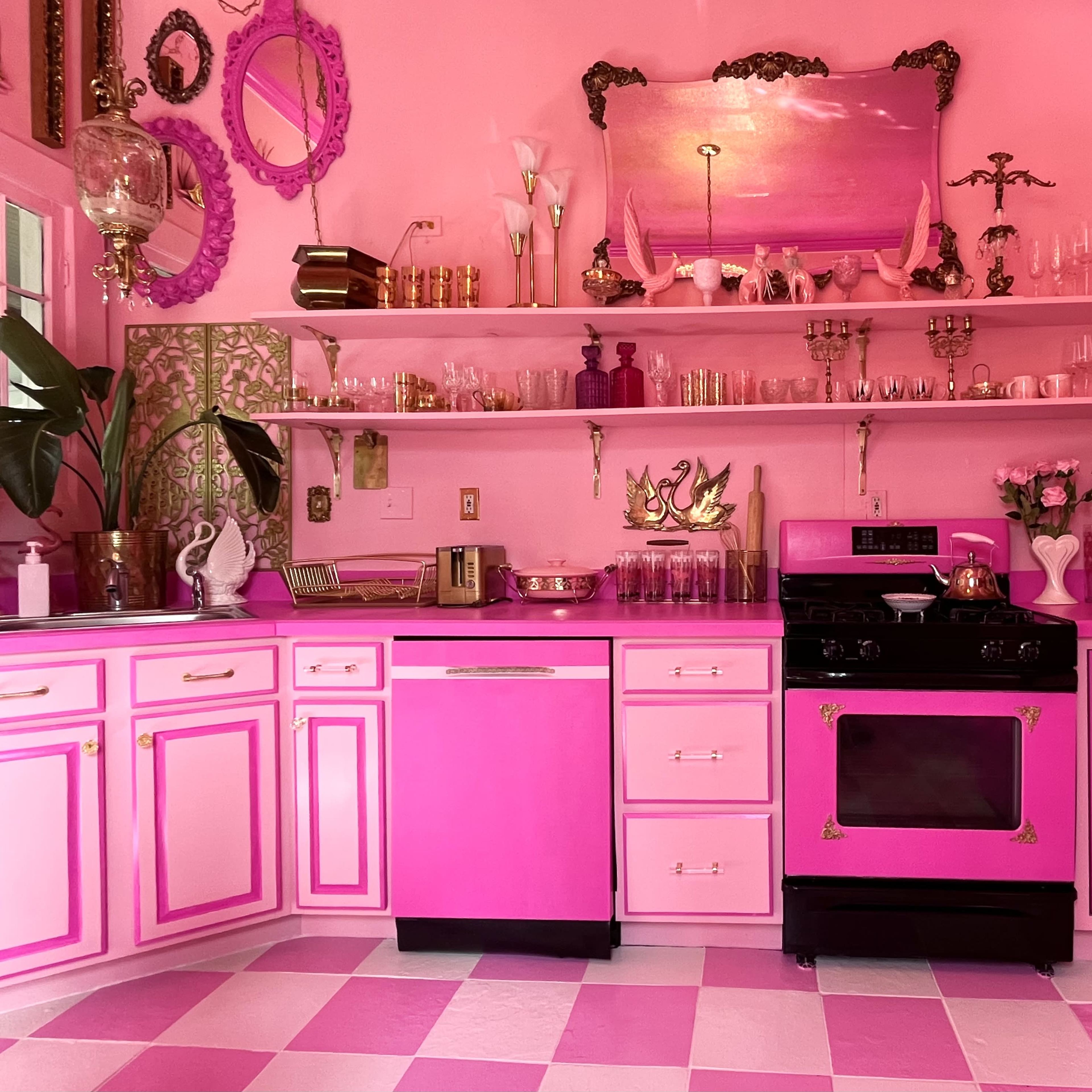 A pink and white kitchen featuring pink cabinets, a black stove, and geometric floor tiles.