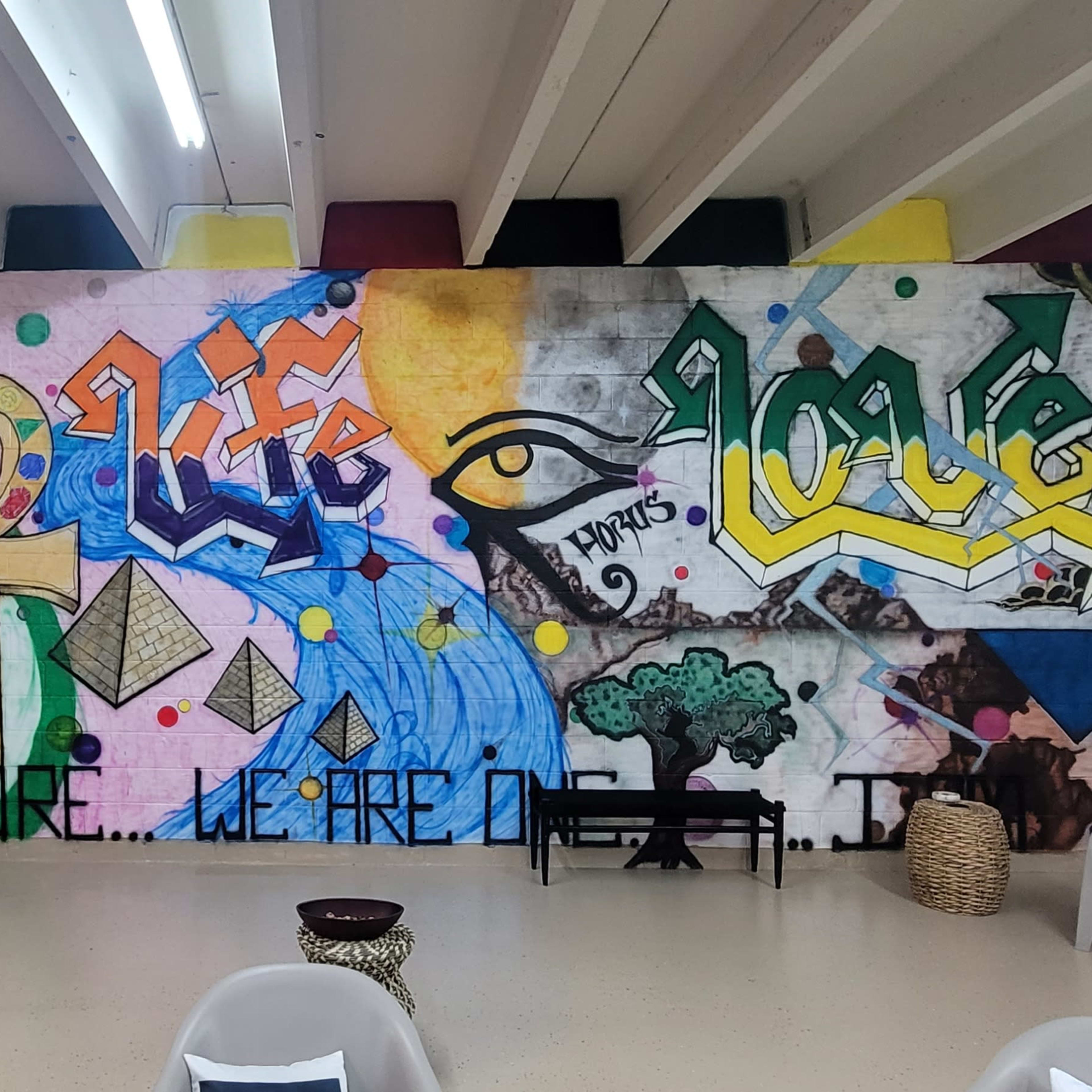 A mural on a wall featuring vibrant graffiti with the words "Rise," "Life," and "Love," along with various symbols and colorful patterns.
