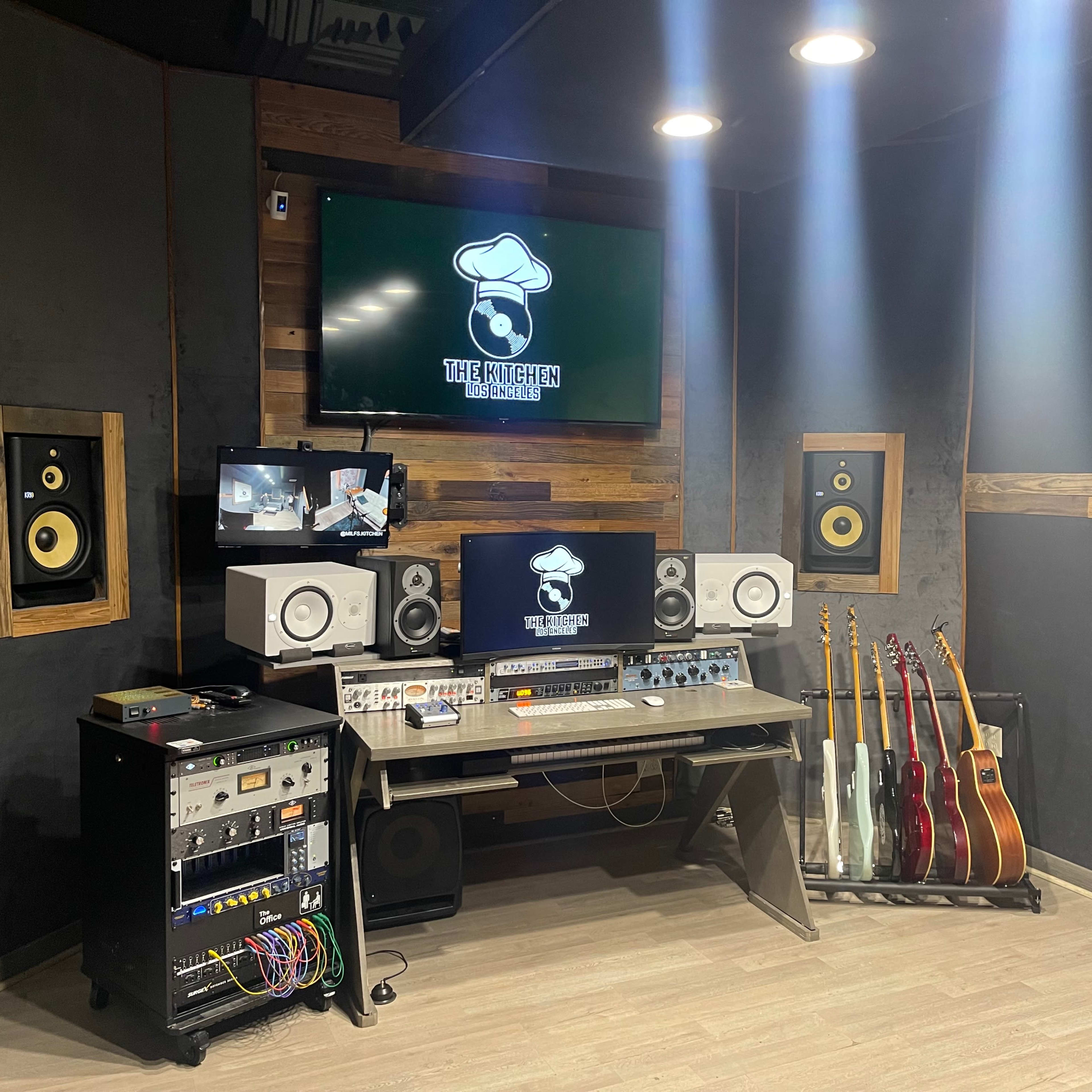 A music studio with a mixing desk, monitors, and various instruments displayed on a rack.