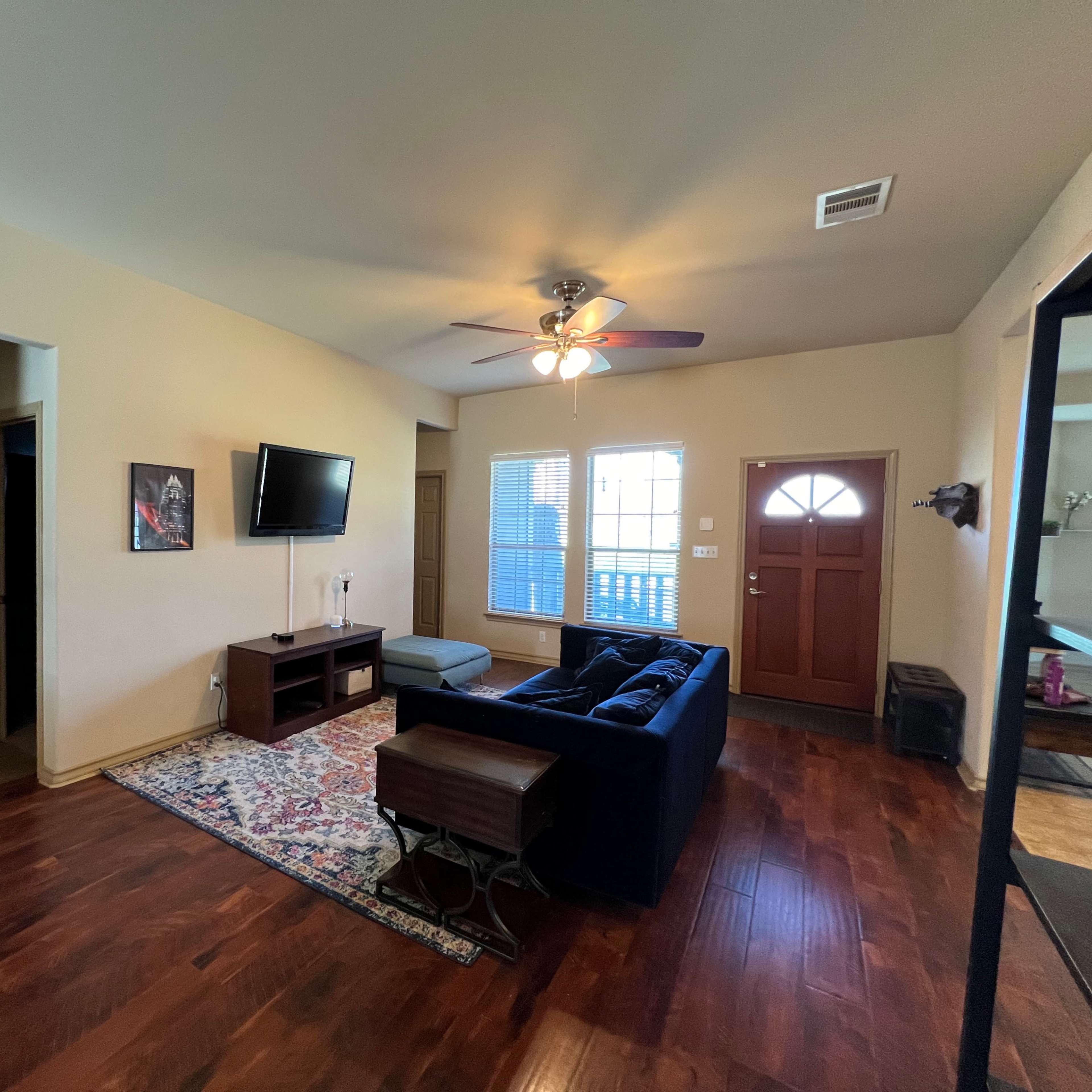 A living room with a dark blue sofa, a television mounted on the wall, and a front door leading outside.