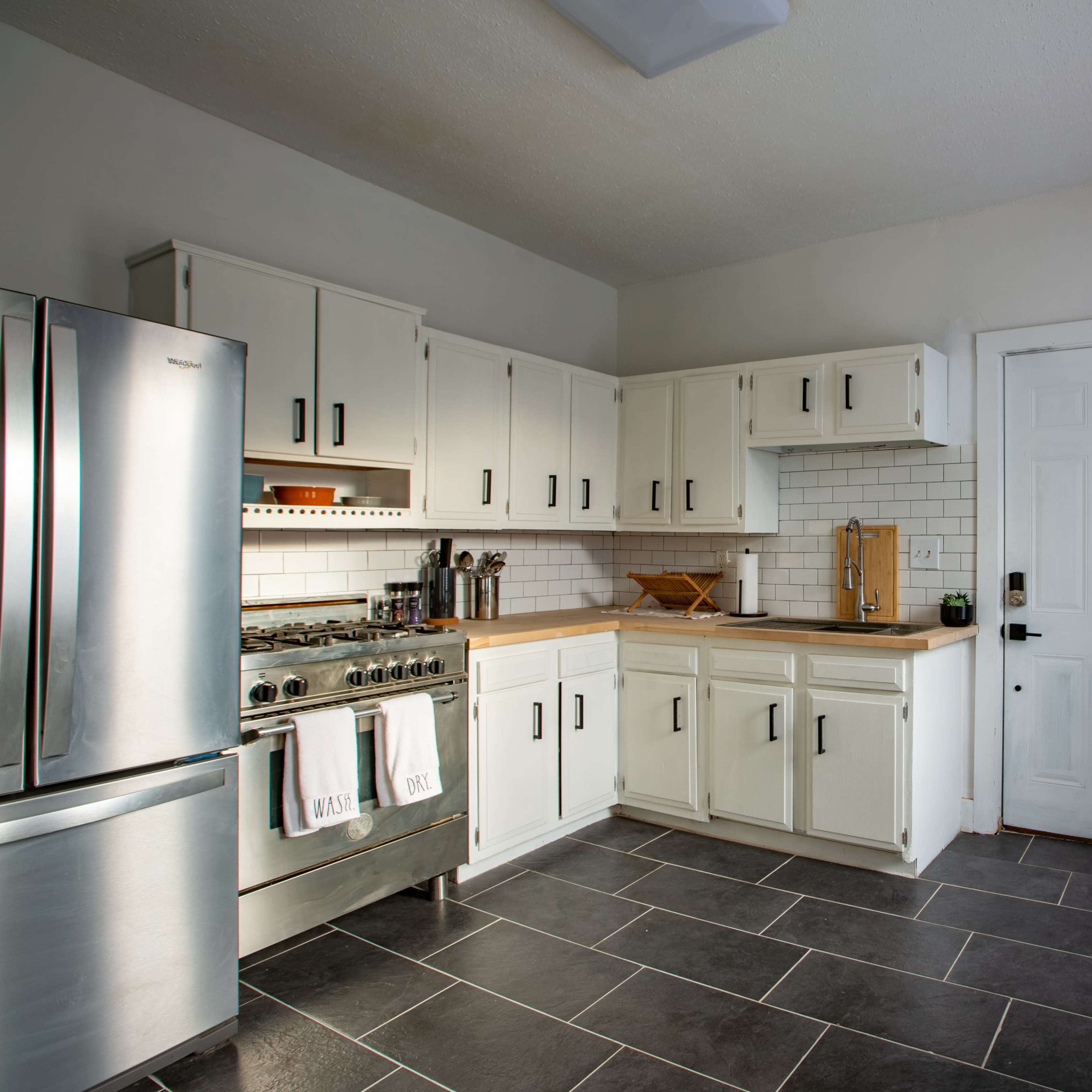 A modern kitchen with white cabinetry, stainless steel appliances, and a tiled floor.