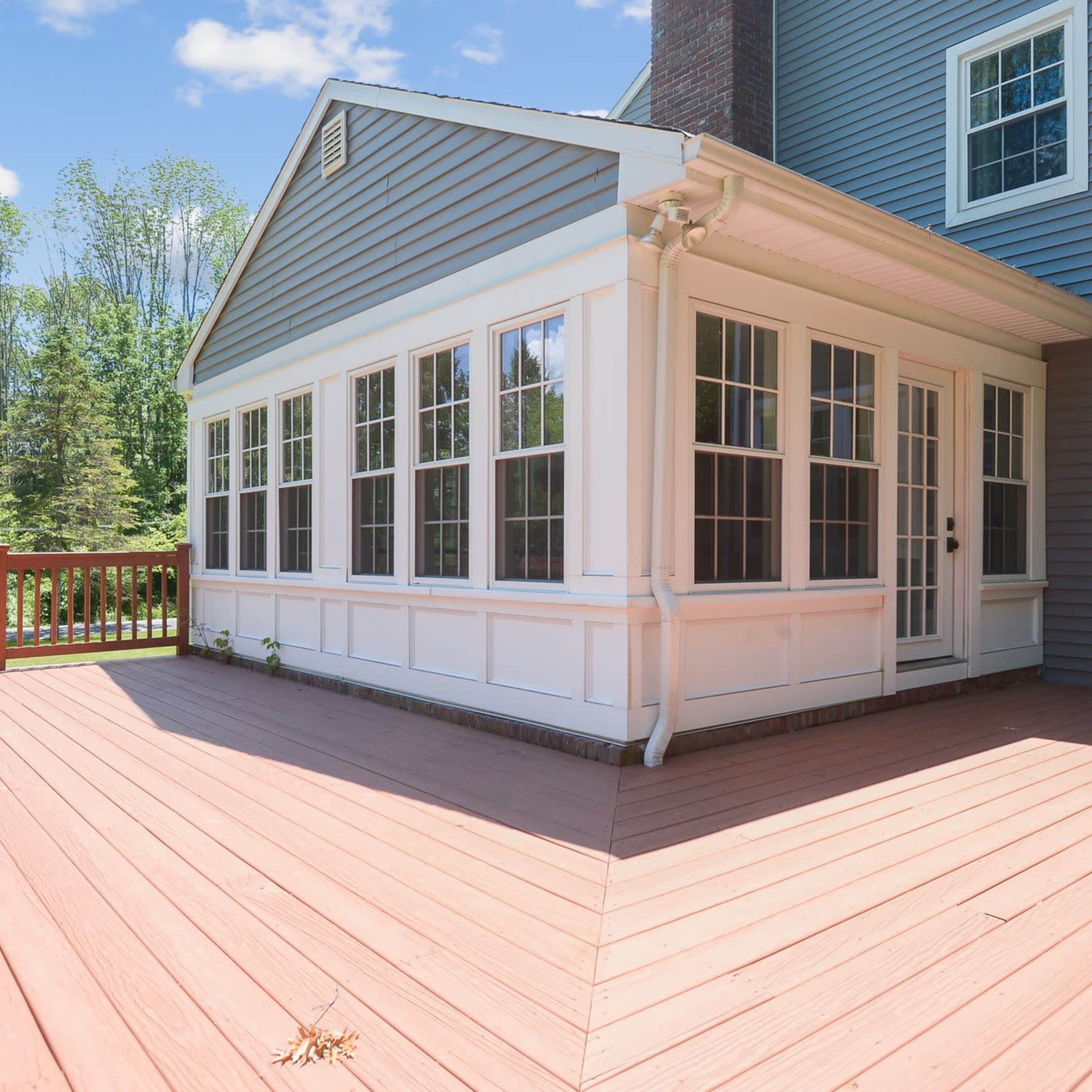 A wooden deck leading up to a gray and white sunroom with multiple windows.