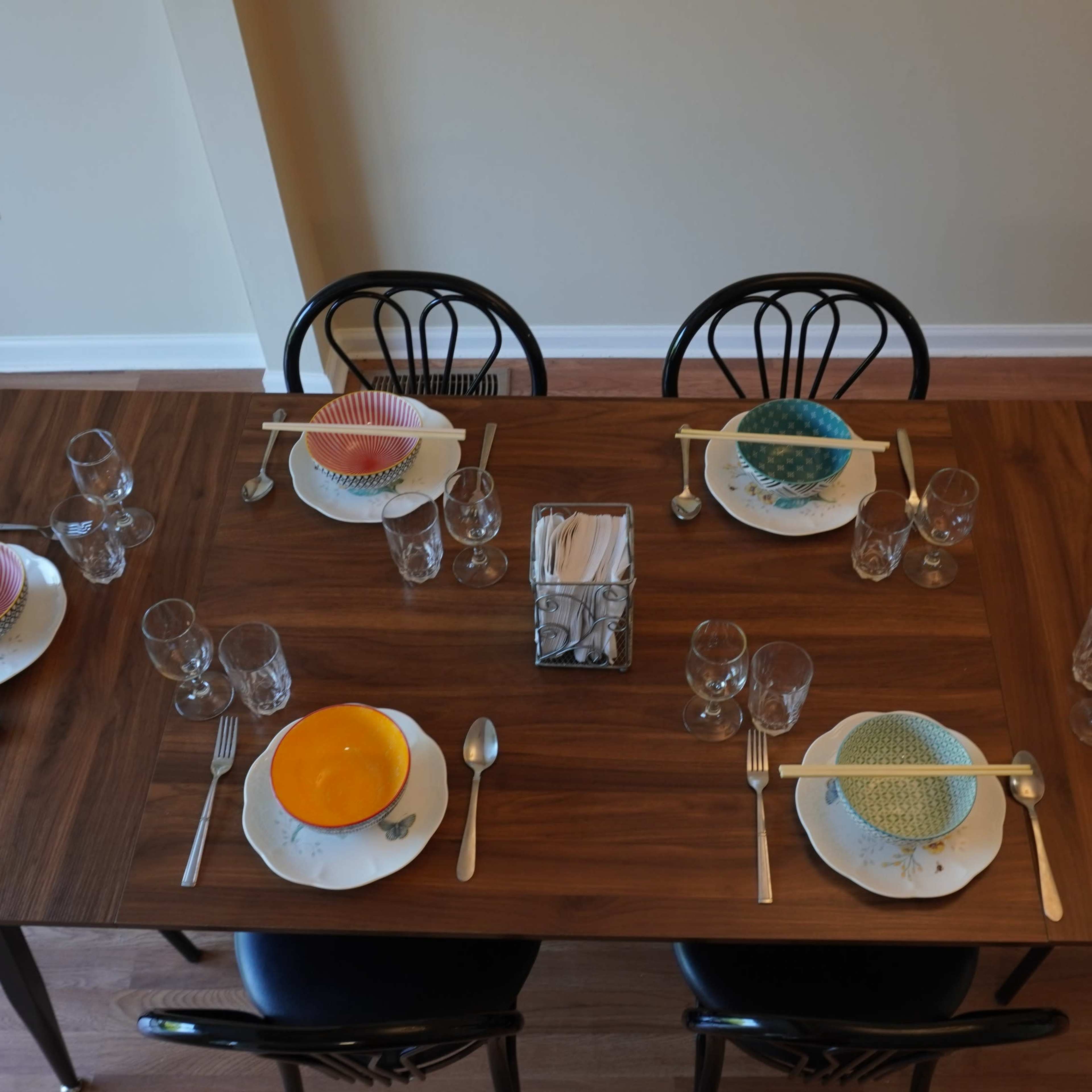 A wooden dining table is set for six, featuring colorful plates and glasses arranged neatly at each place setting.