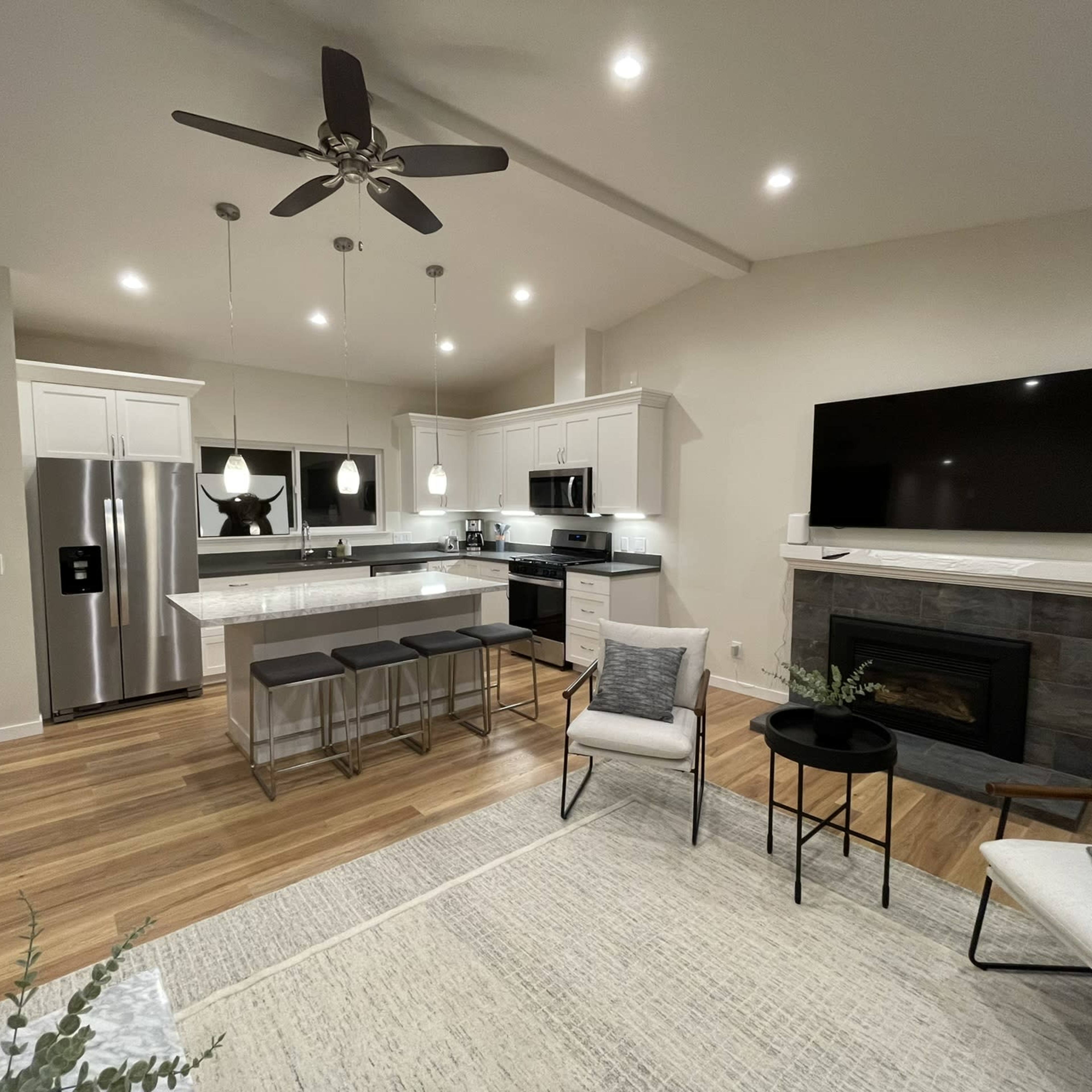 A modern kitchen and living area featuring a stainless steel refrigerator, an island with seating, a fireplace, and a television mounted on the wall.