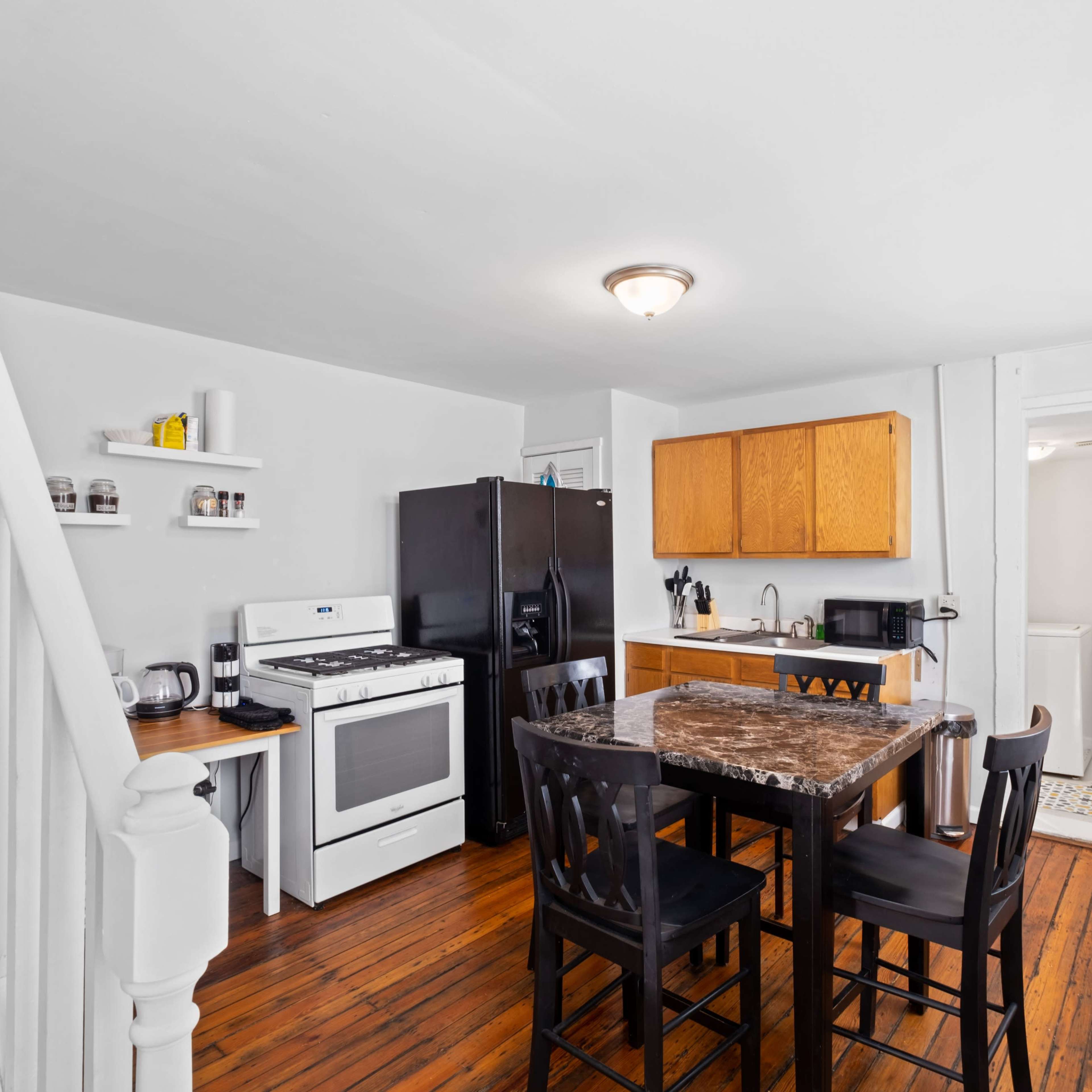 The kitchen features a black refrigerator, white stove, wooden cabinetry, and a dining table with four chairs on a wooden floor.