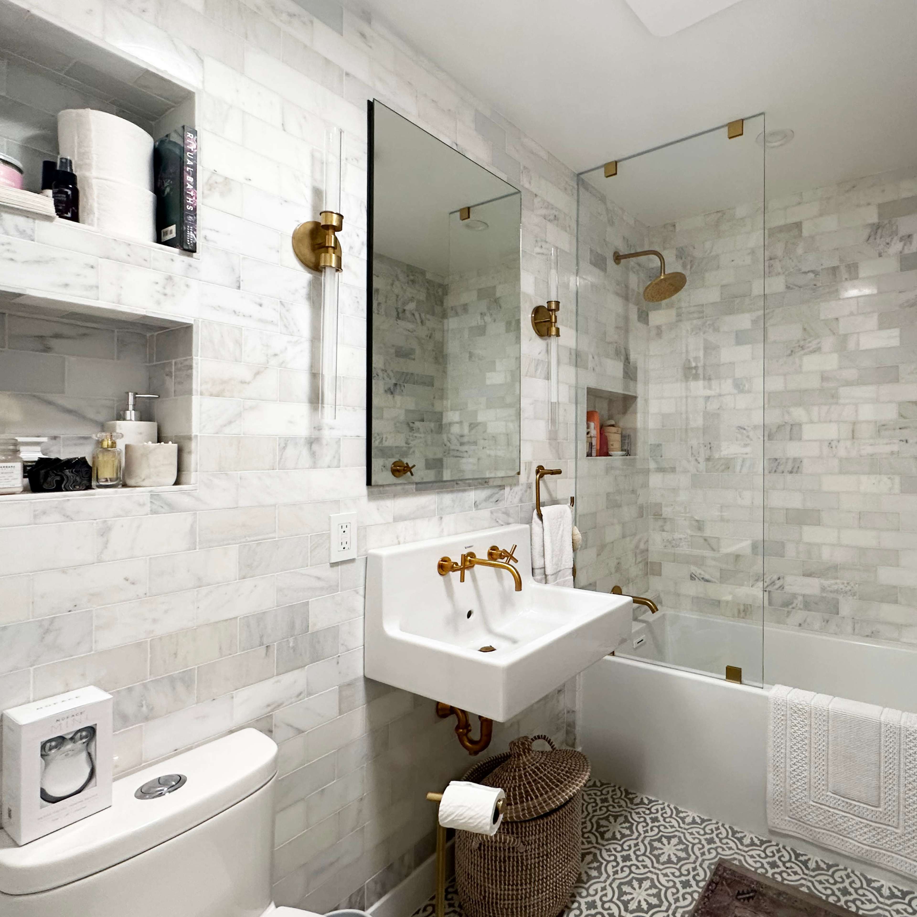 The bathroom features a marble-tiled shower area, a white sink with gold fixtures, and organized toiletries on shelves.