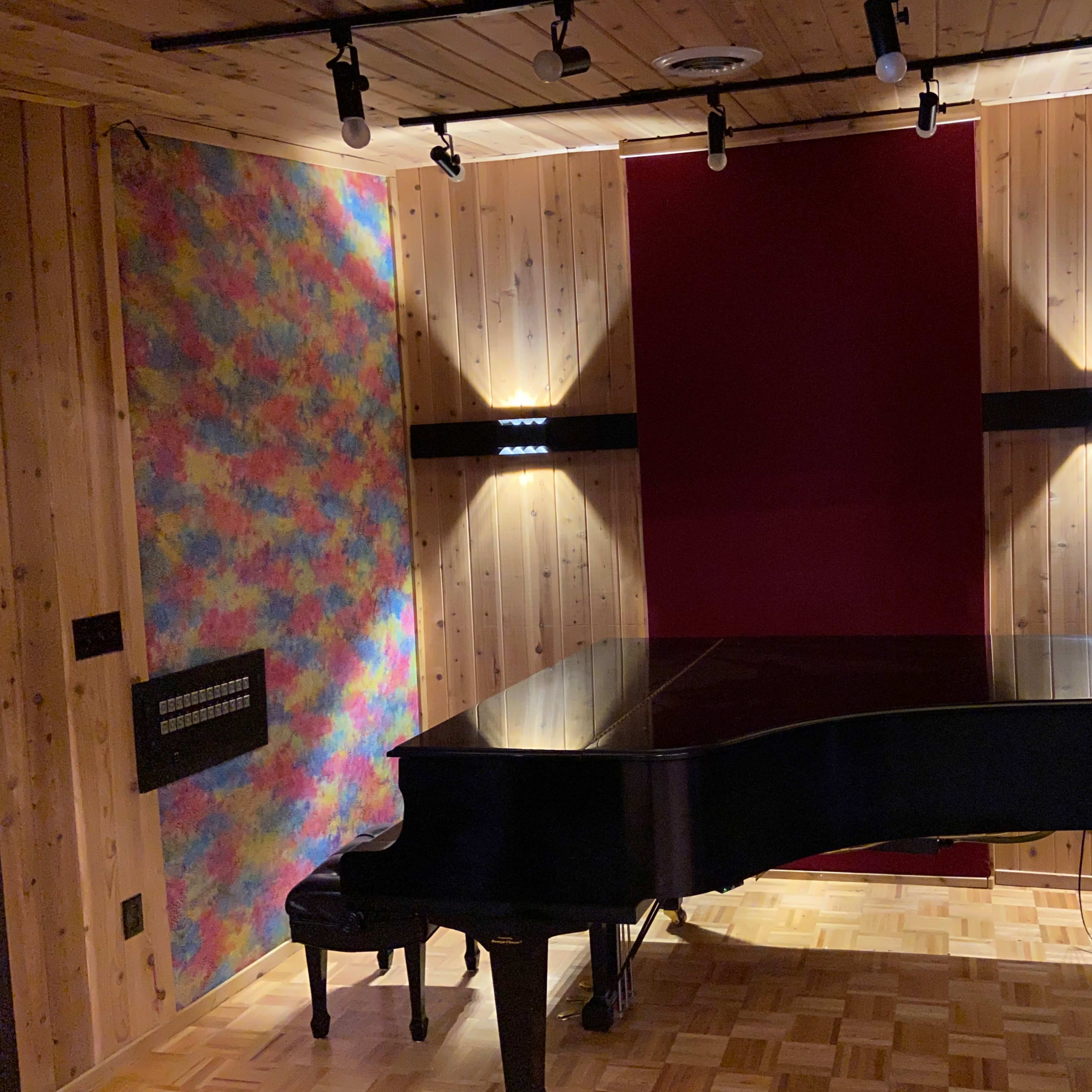 A grand piano positioned in a wooden room with colorful wall accents and ceiling lights.