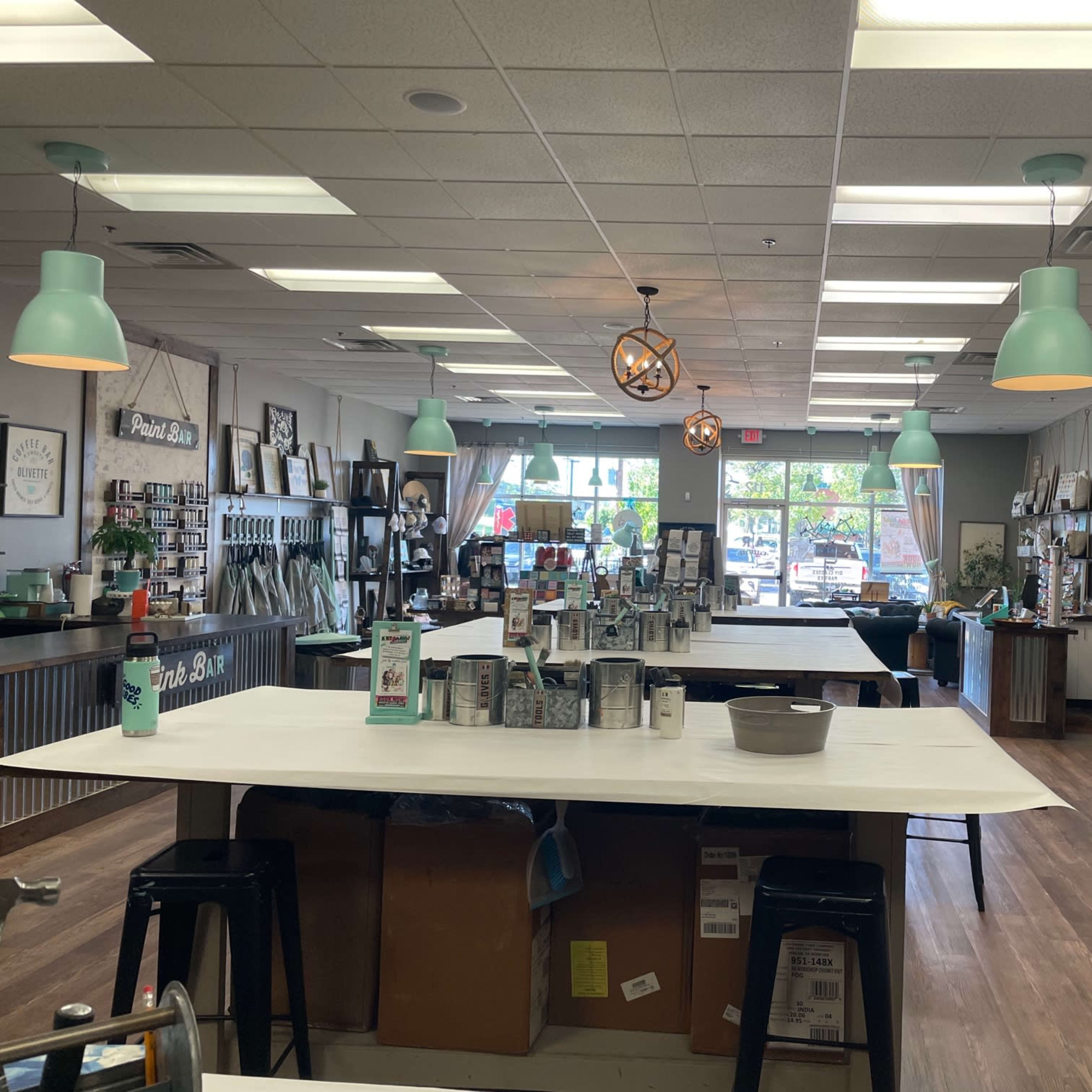 A spacious craft studio with tables, shelves of supplies, and large windows allowing natural light to enter.