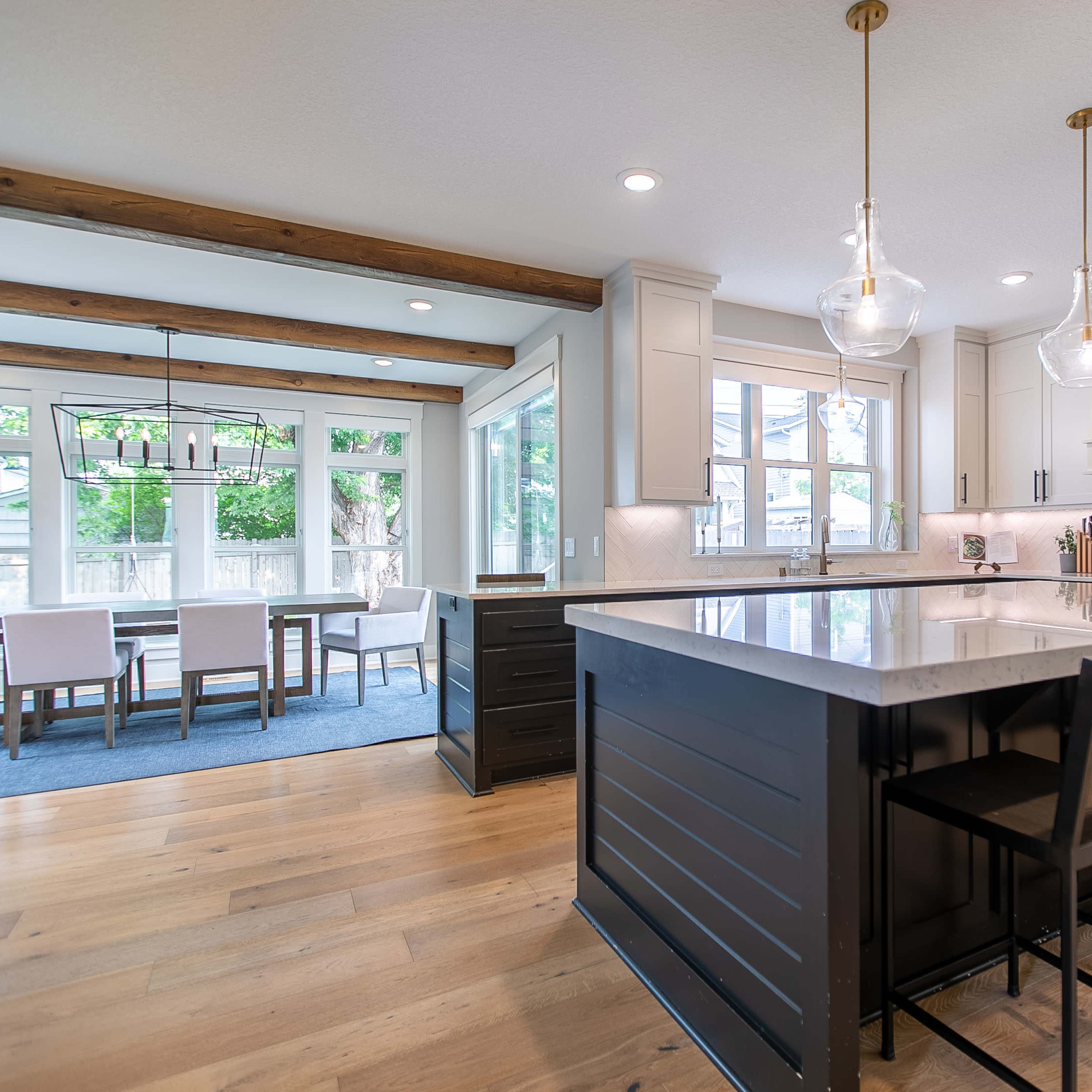 A modern kitchen featuring a large island with bar stools, sleek cabinetry, and a dining area visible through large windows.
