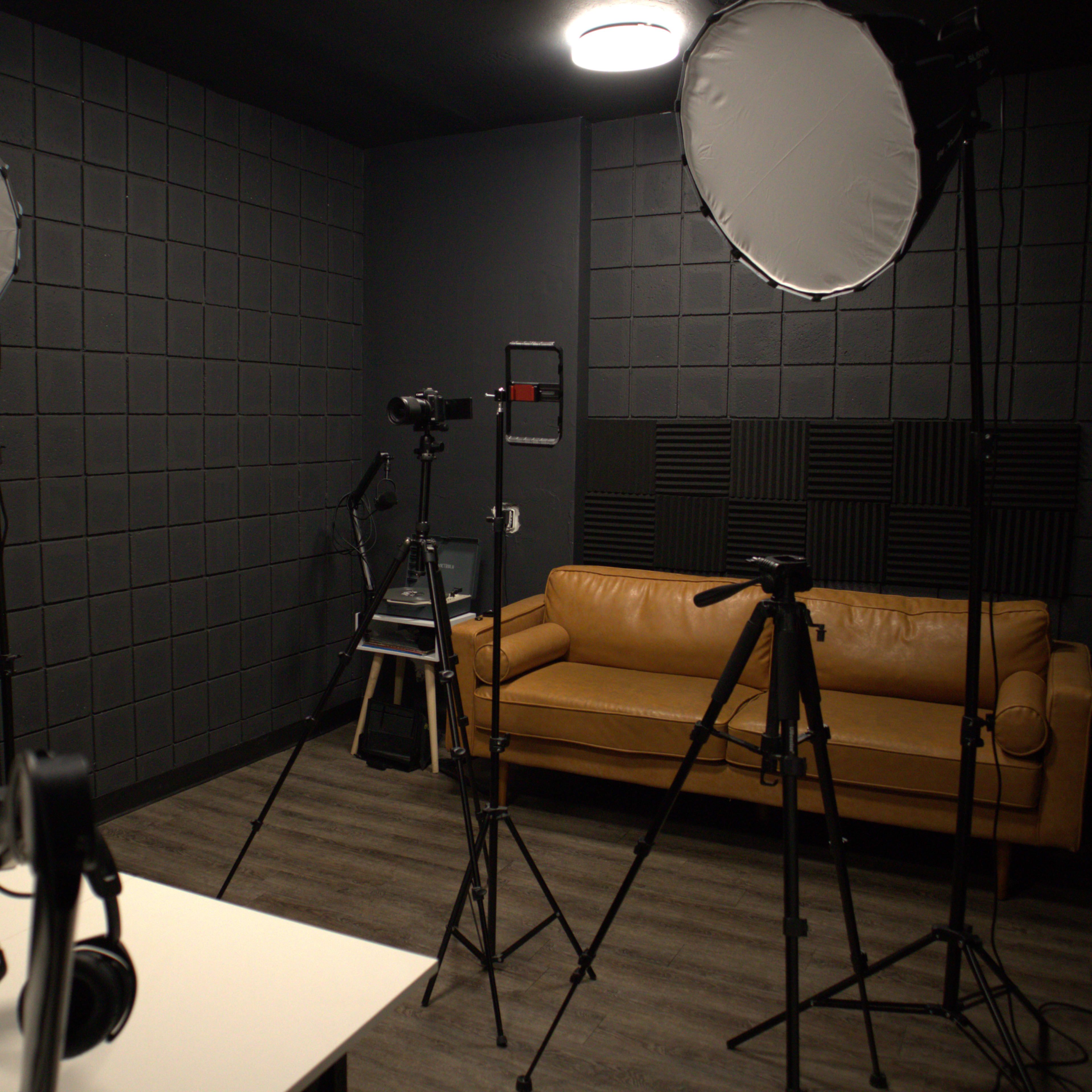 A photography studio with a tan couch, tripods, lighting equipment, and headphones arranged in a dark room.