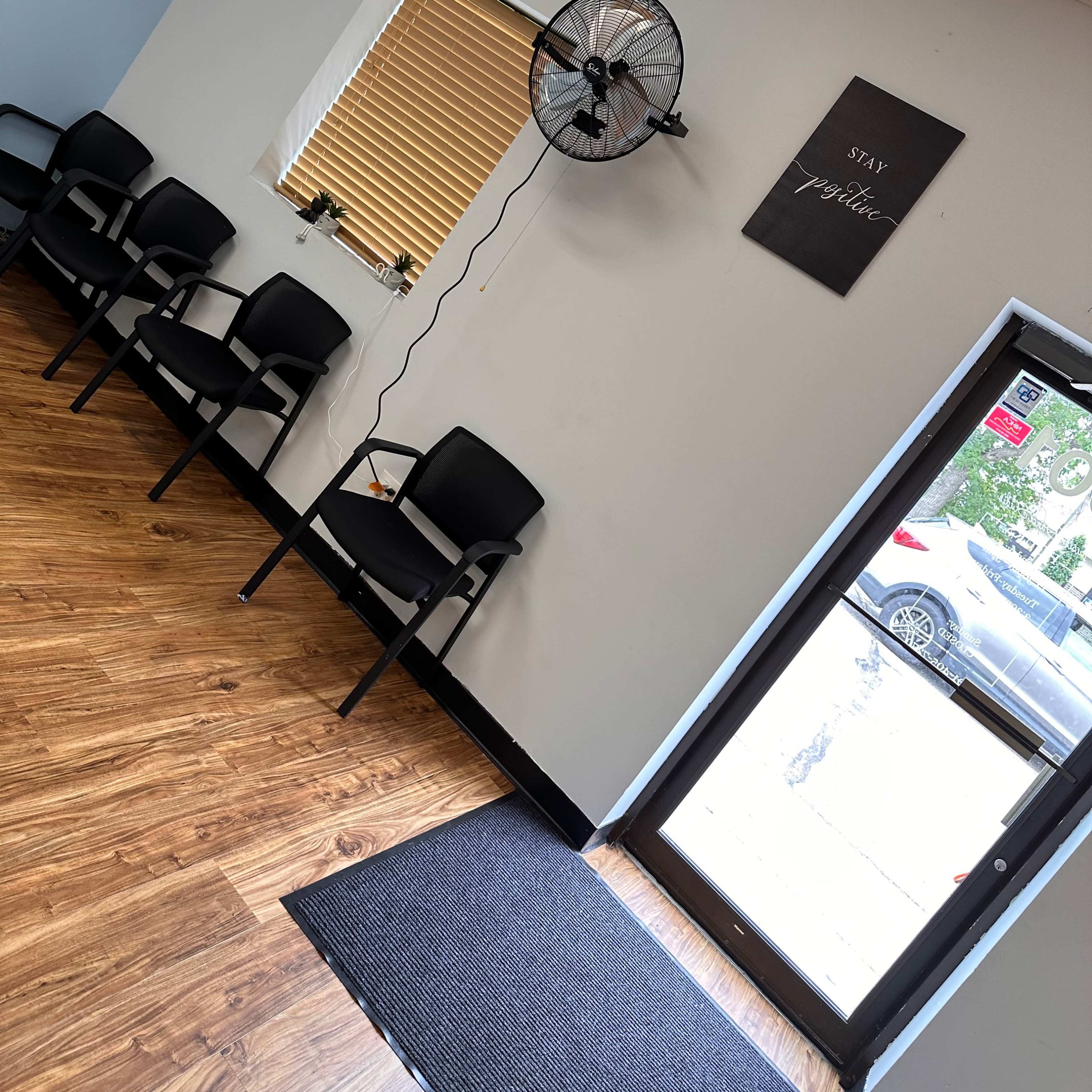 A waiting area with several black chairs, a wall-mounted fan, and a door leading outside, along with motivational signs on the walls.