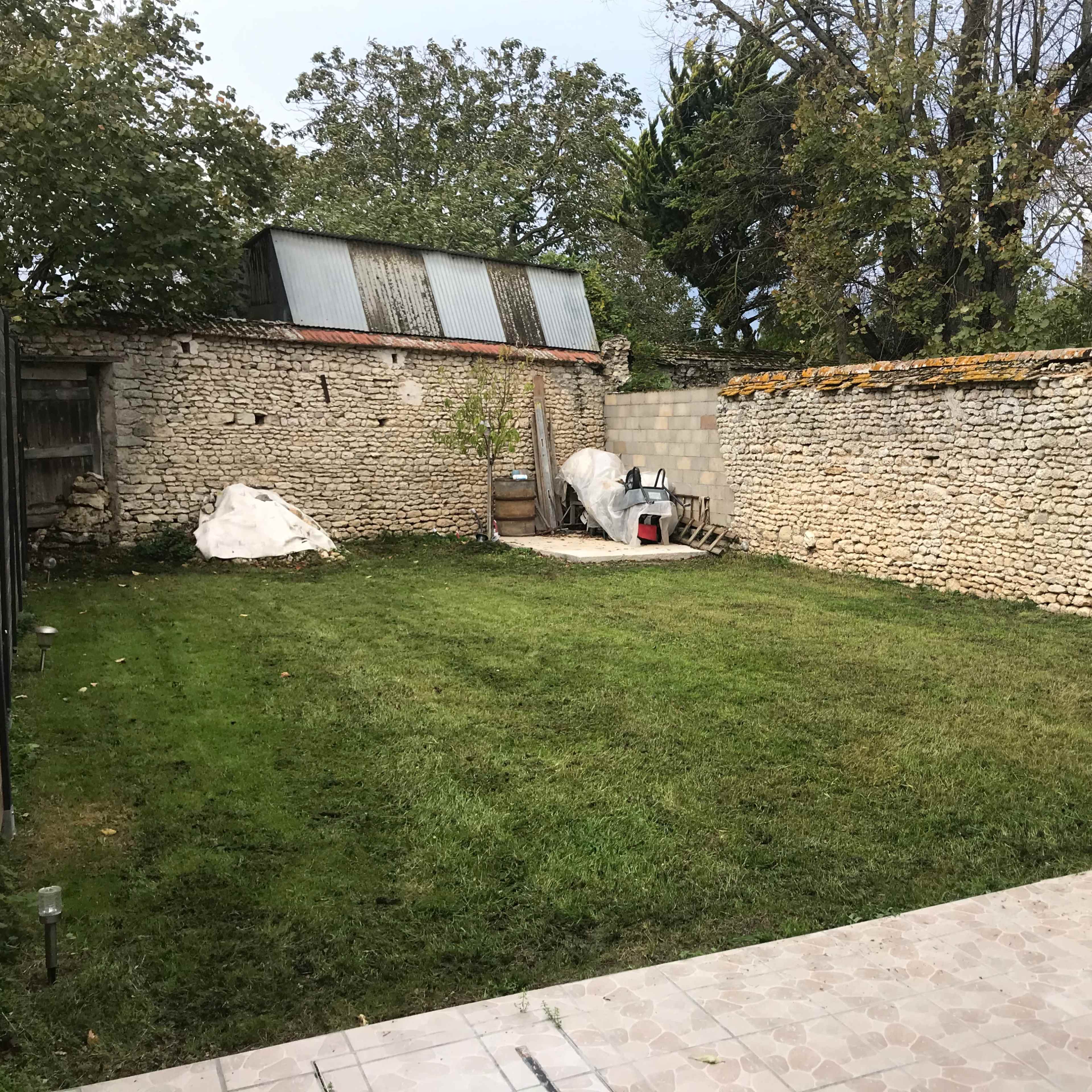 A spacious garden enclosed by stone walls, featuring a grassy area and a decorative sculpture resembling a wolf.