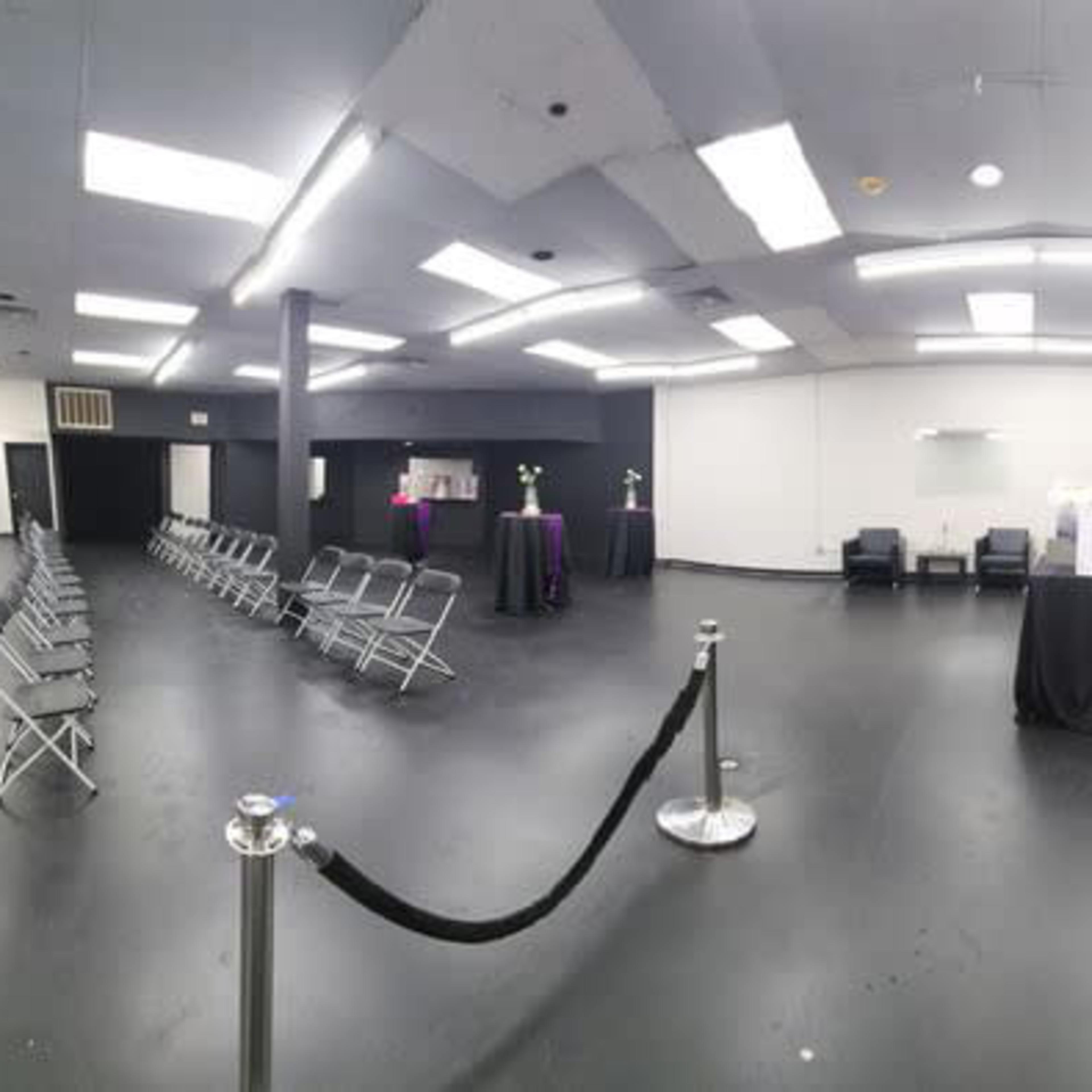 A spacious, empty room with rows of metal chairs facing a central area and several tables along the walls.