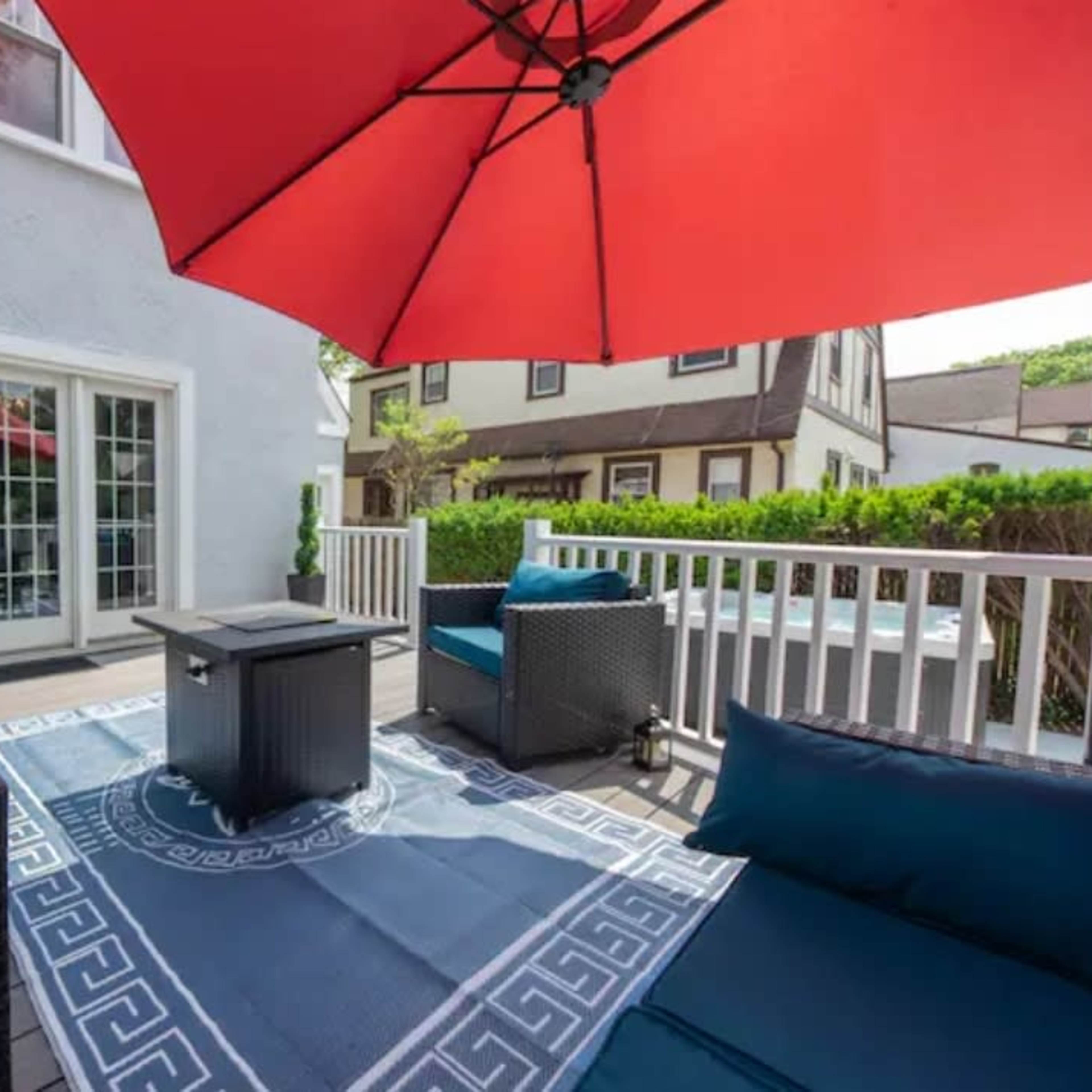 A patio area features wicker seating with blue cushions, a red umbrella, and a small table on a decorative rug.