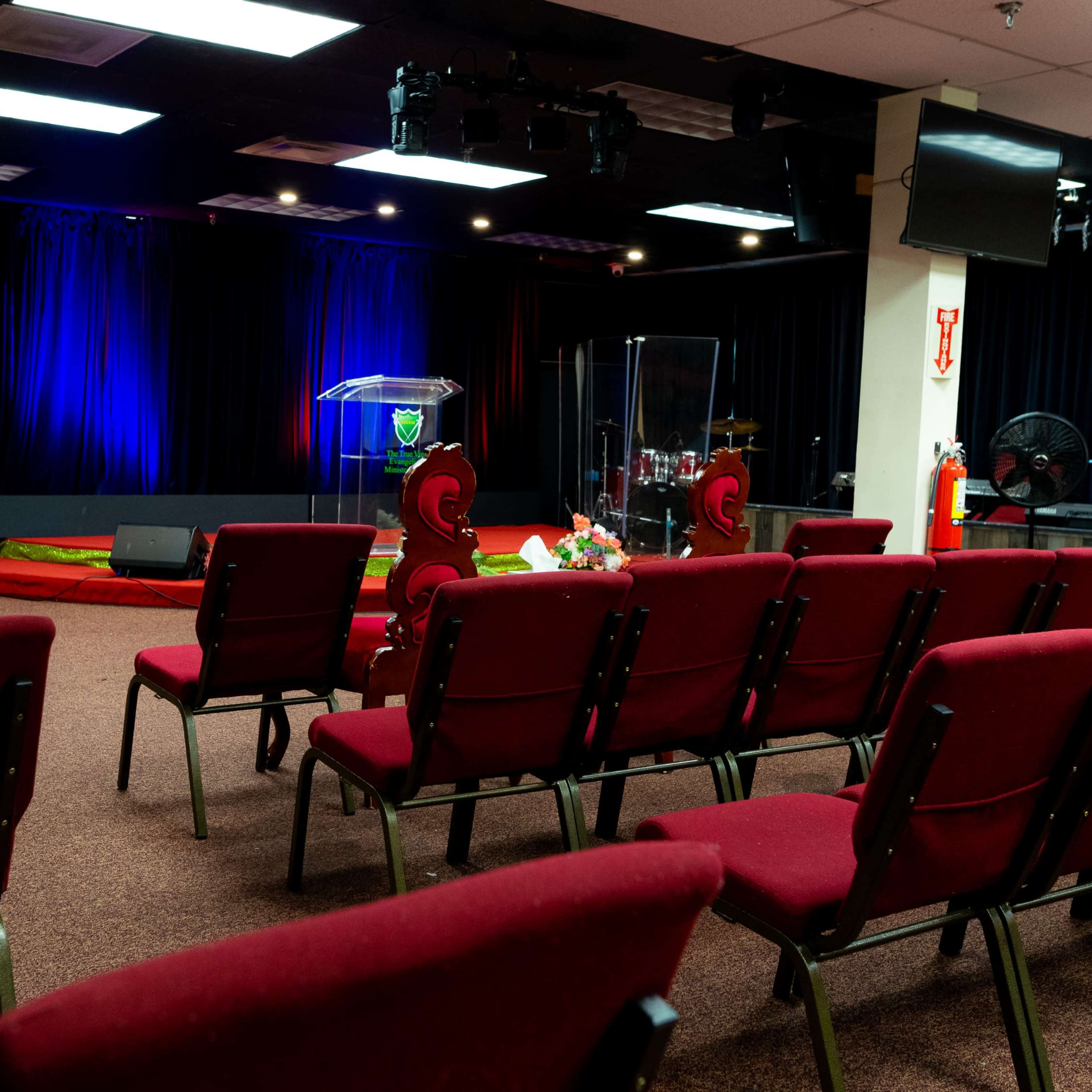 A church sanctuary with rows of red chairs facing a transparent podium and a drum set in the background.