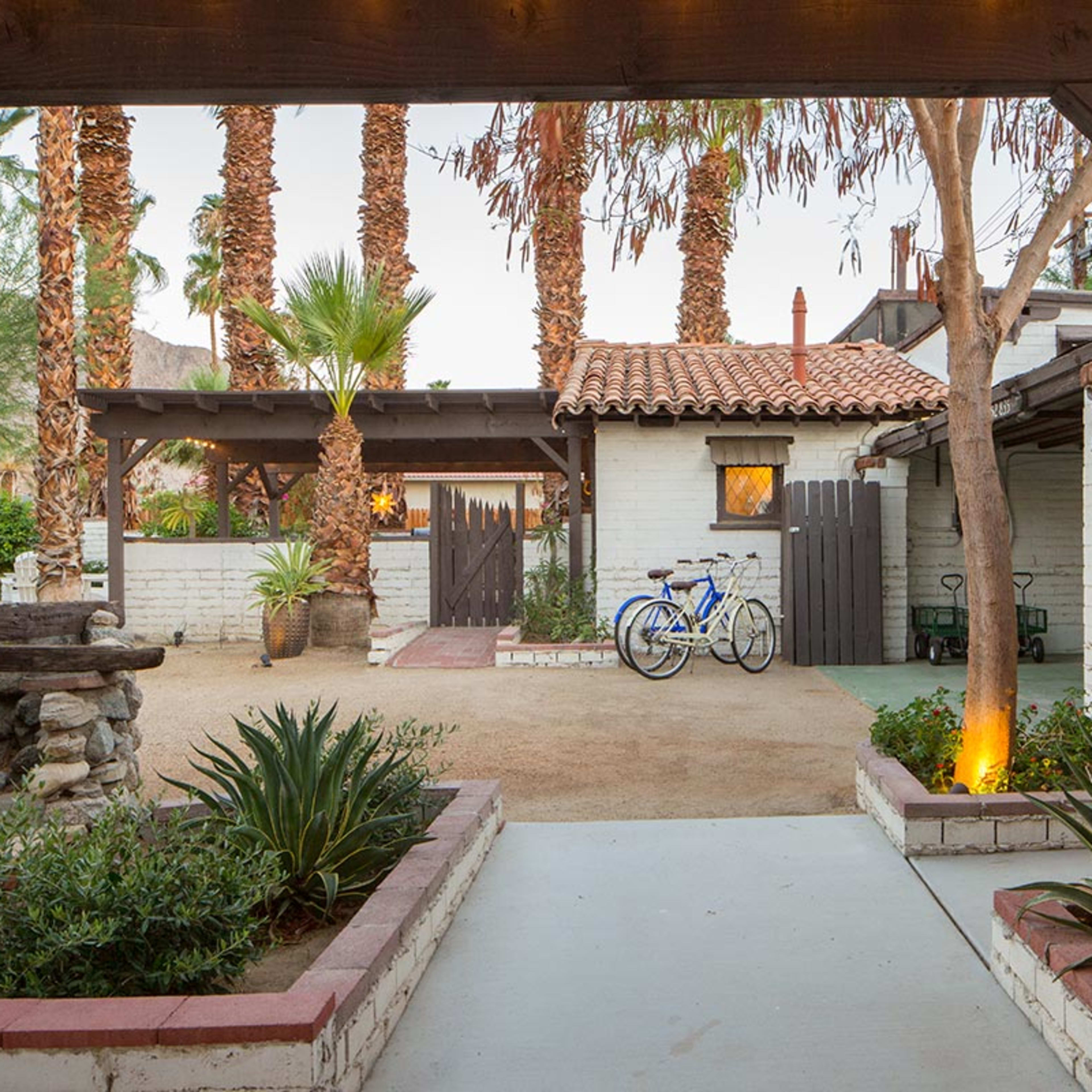 A peaceful courtyard with palm trees, a gravel path, and bicycles parked near a white brick building.