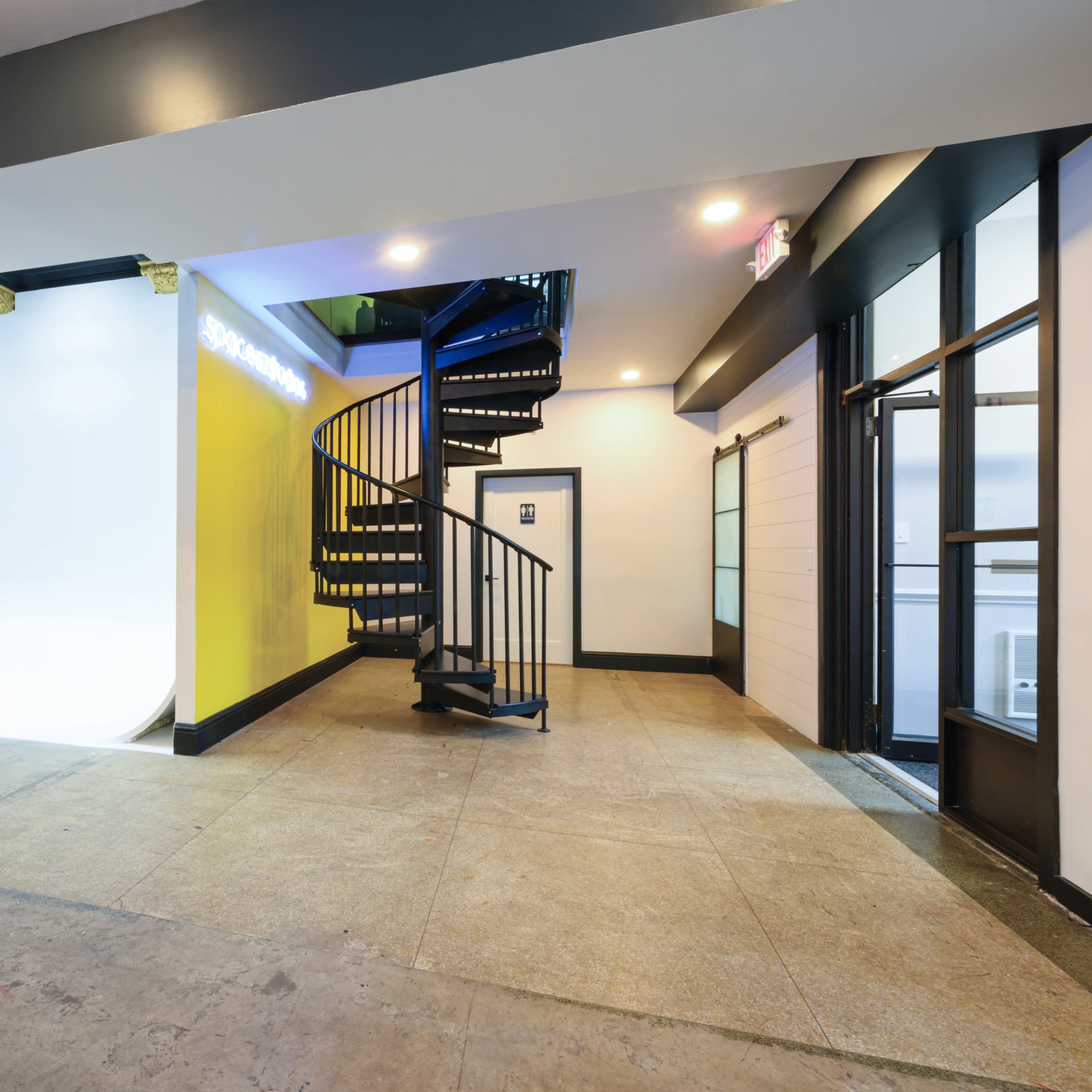 A spacious interior with a spiral staircase leading to an upper level, one wall painted bright yellow, and an open doorway on the right.