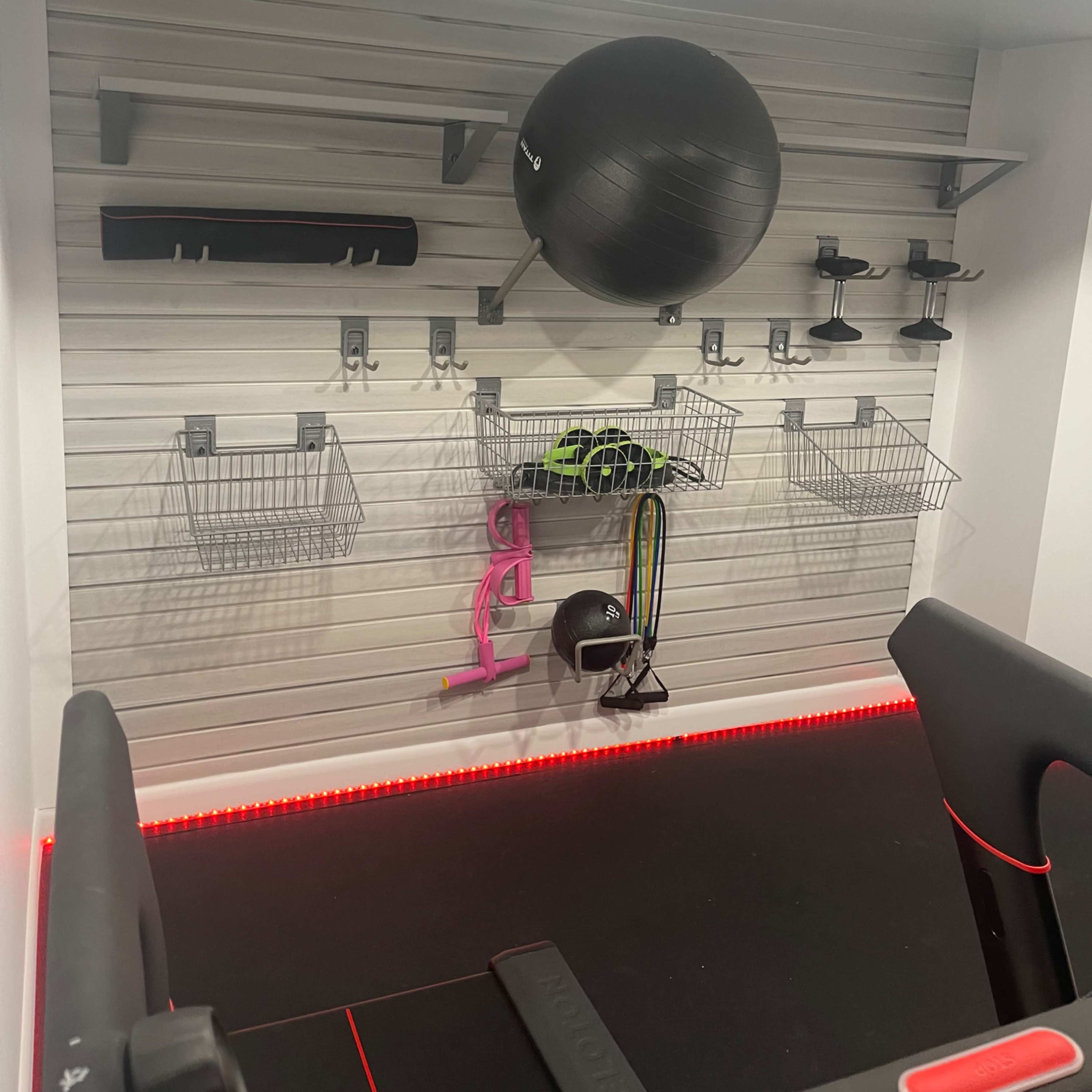 A home gym wall organized with exercise equipment, including a stability ball, shelves, and wire baskets for storage.