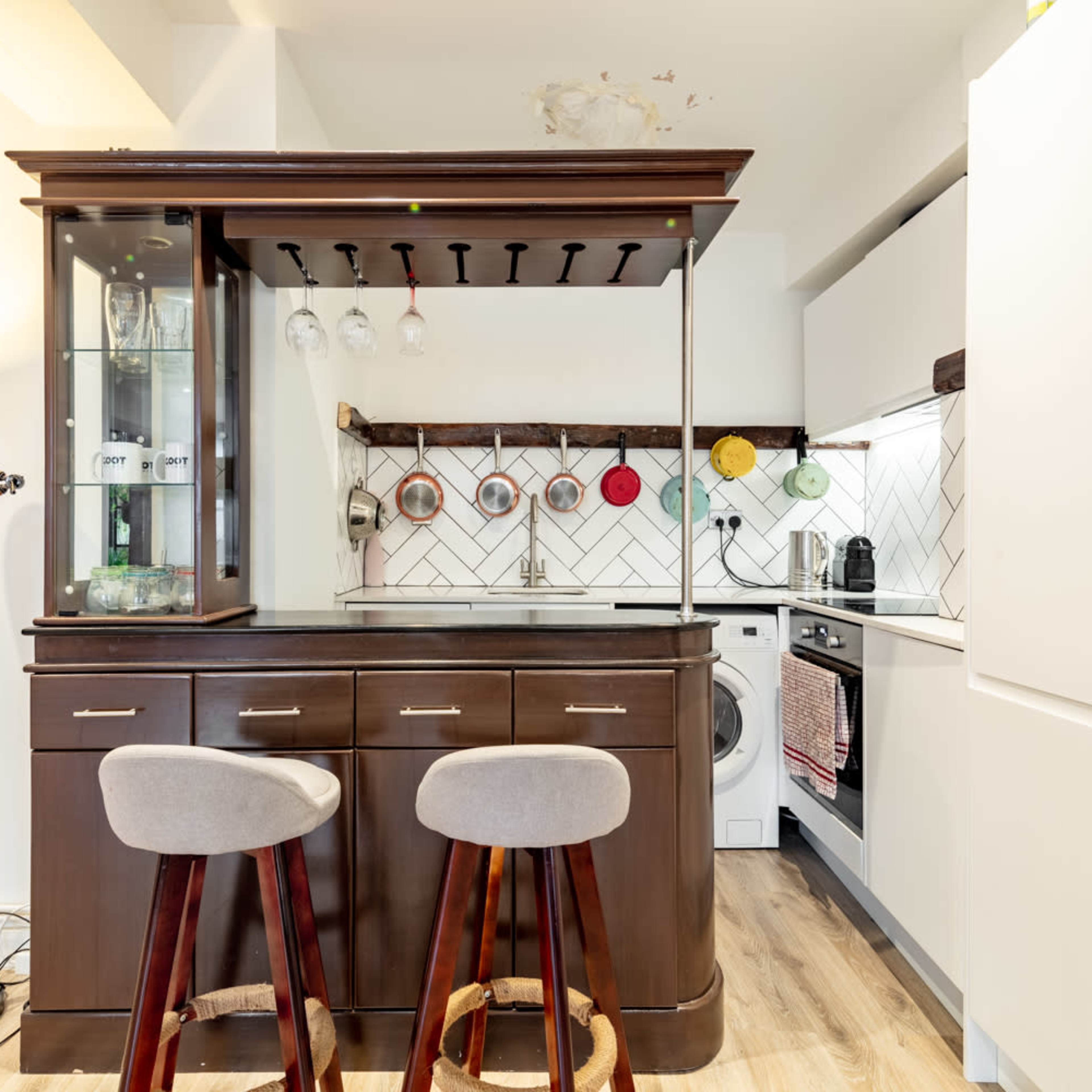 A modern kitchen with a dark wooden island featuring two bar stools and a wall of kitchen utensils and appliances.