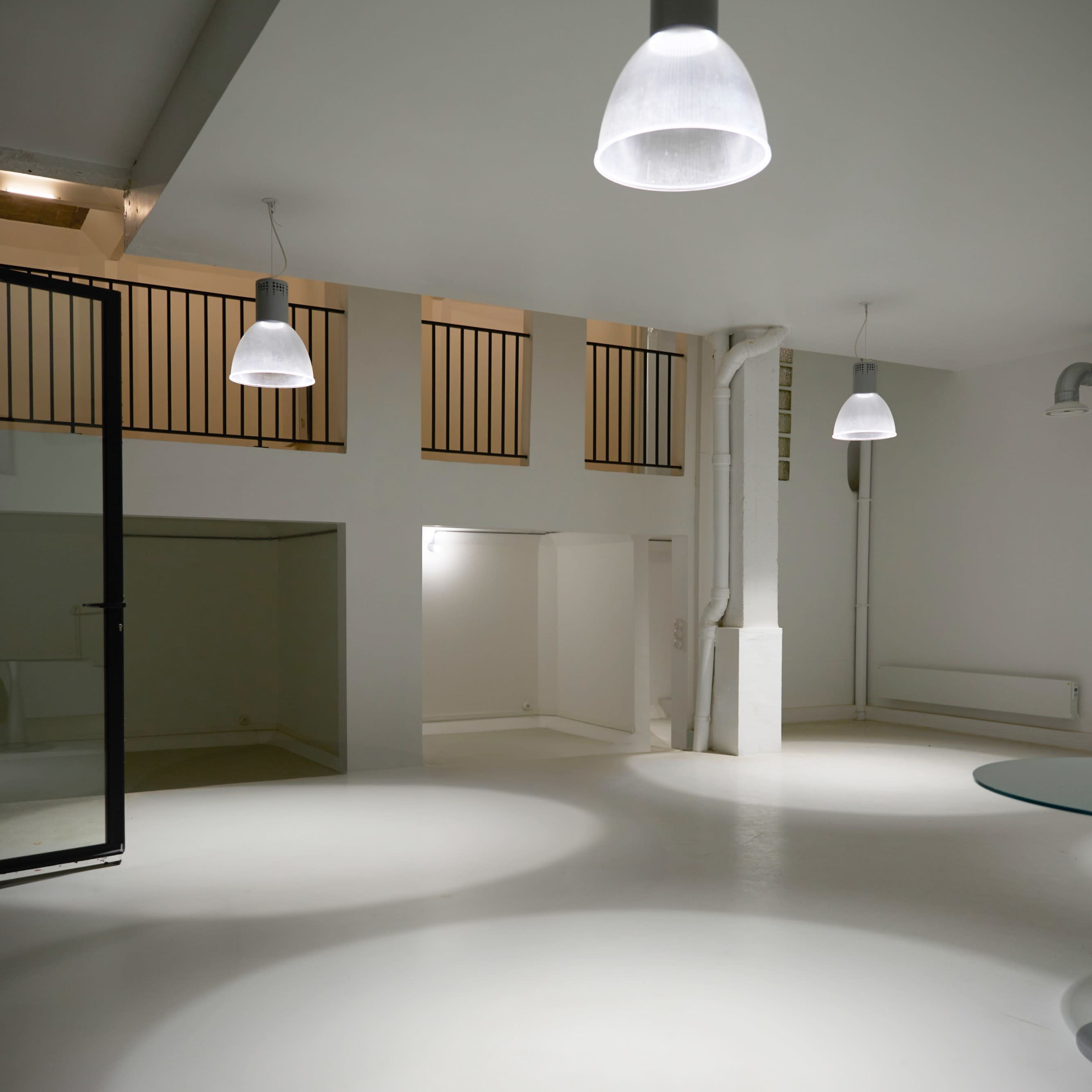 A minimalist, open interior space with white walls, a smooth floor, and several pendant lights hanging from the ceiling.