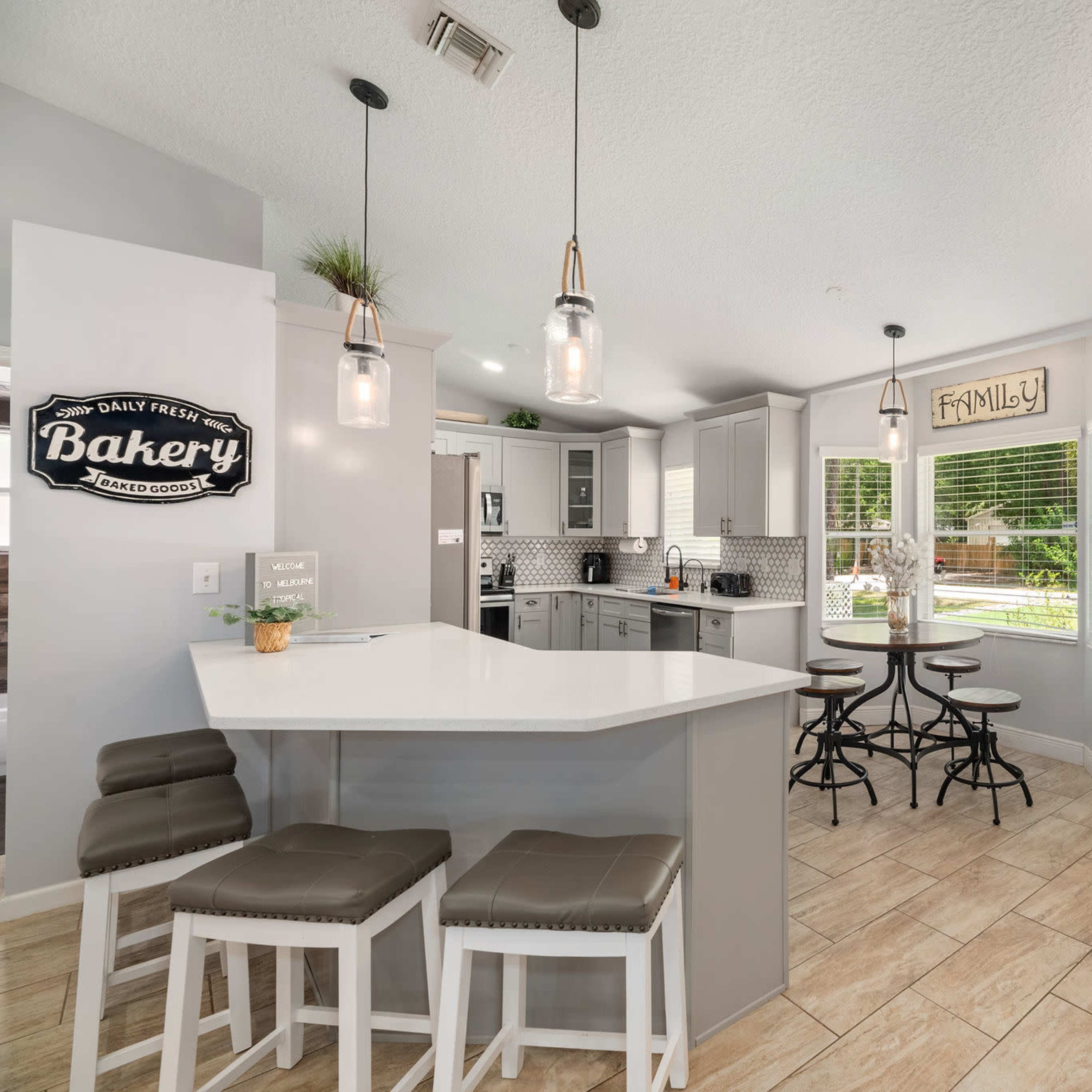 A modern kitchen features a white island with bar seating, gray cabinets, and a dining area, with a door leading to the outside.