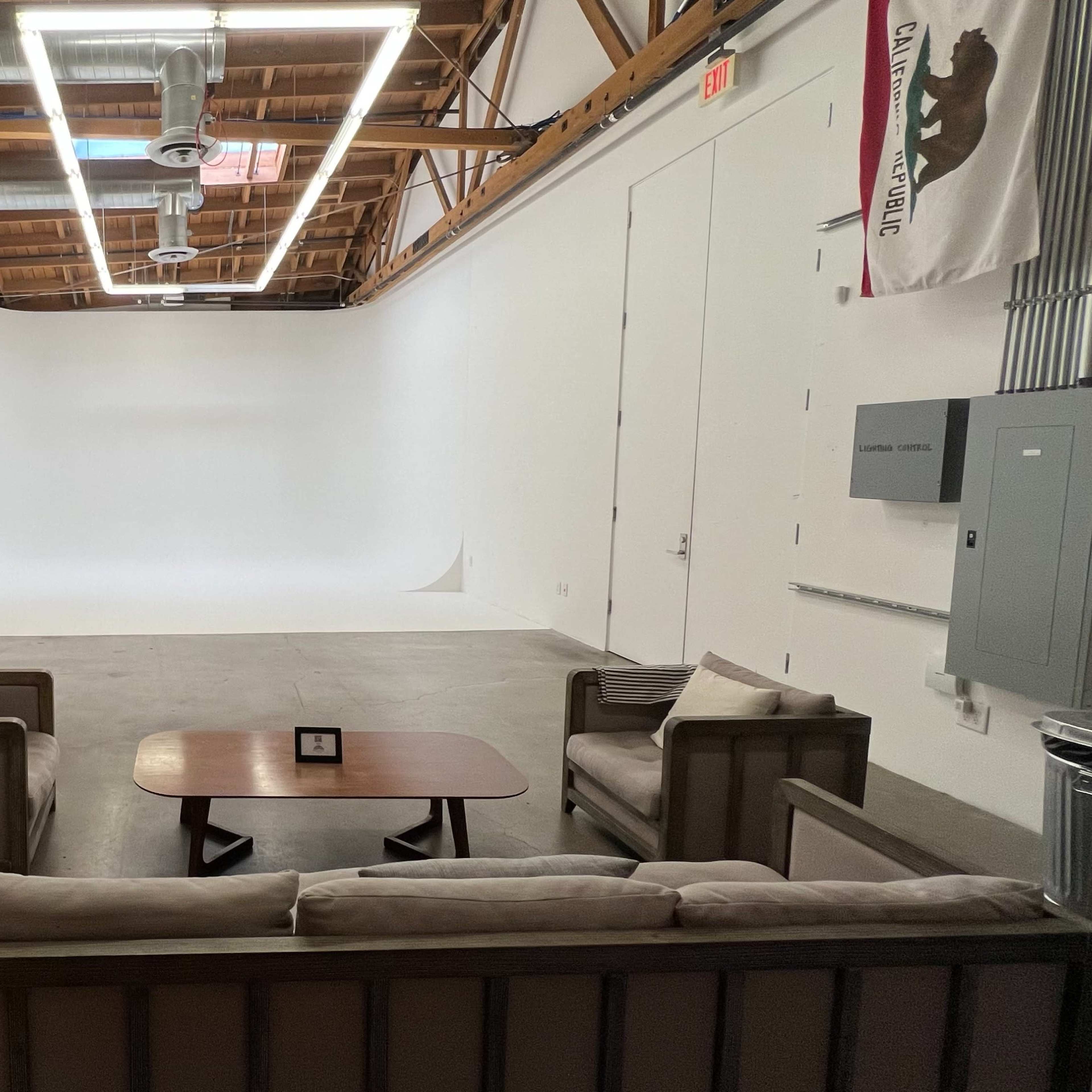 A spacious studio with a seating area including a sofa and table, and a large white backdrop in the background.