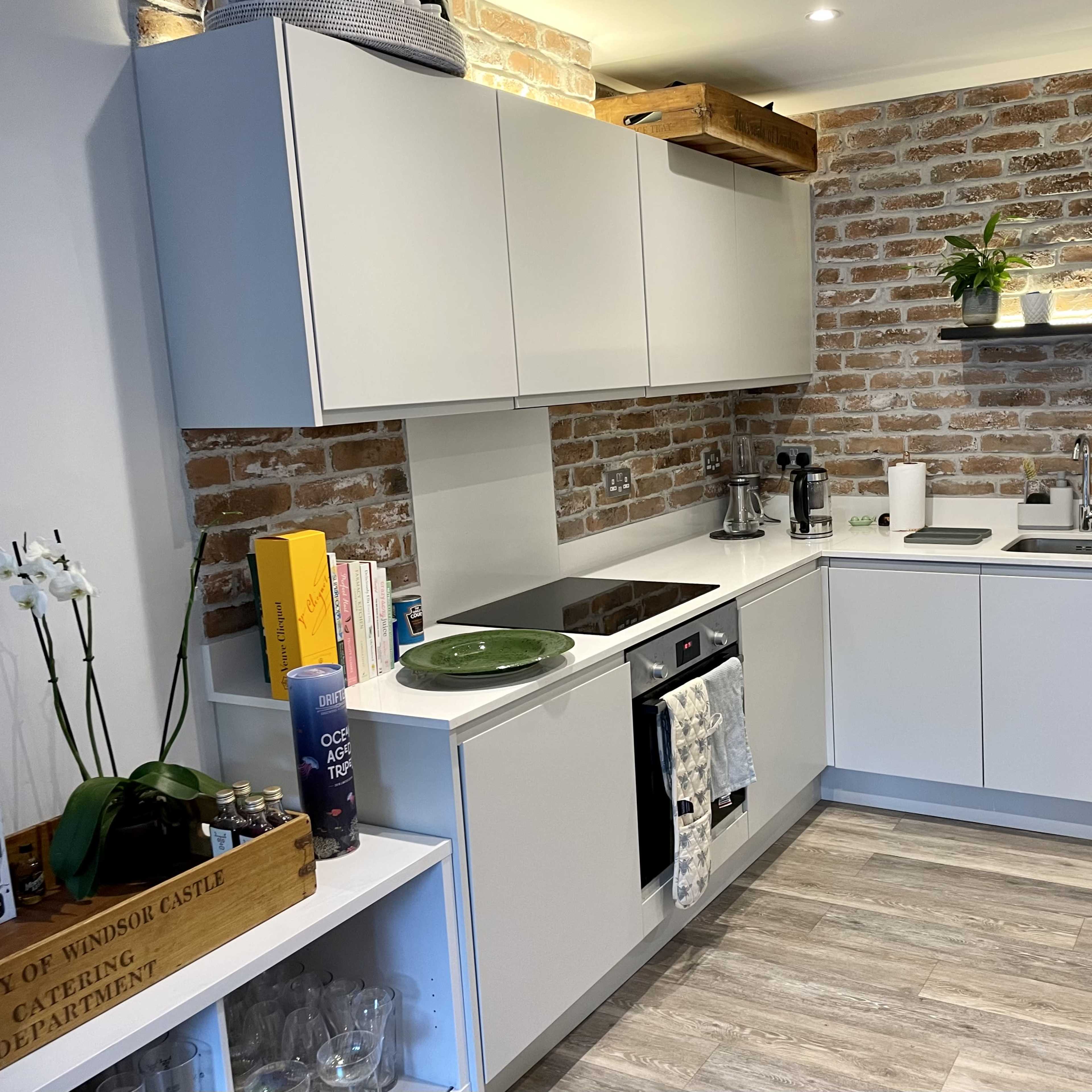 A modern kitchen with white cabinets, a brick wall, and a countertop featuring various appliances and plants.