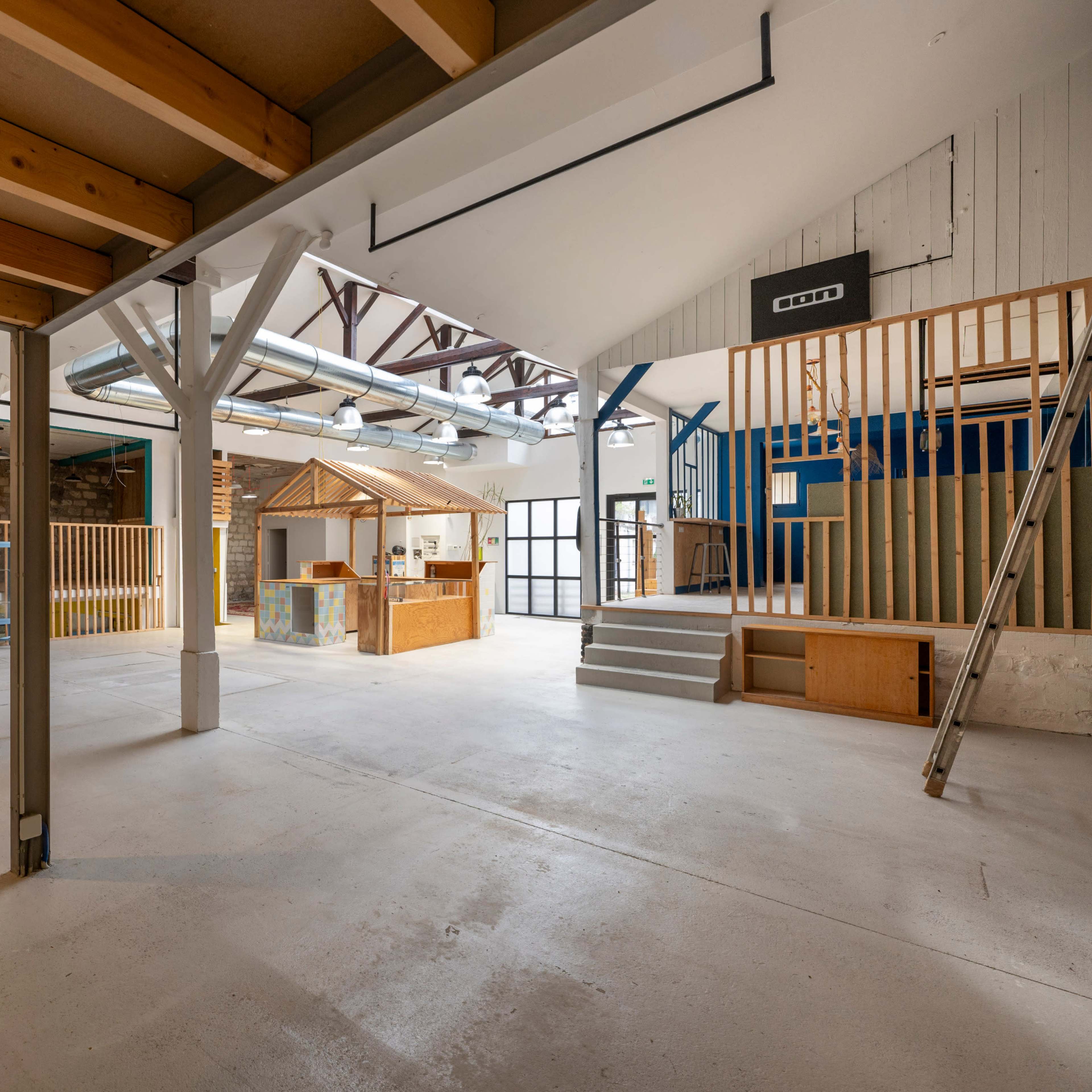 An open, spacious interior of a renovated building with wooden beams, various structures, and staircases.