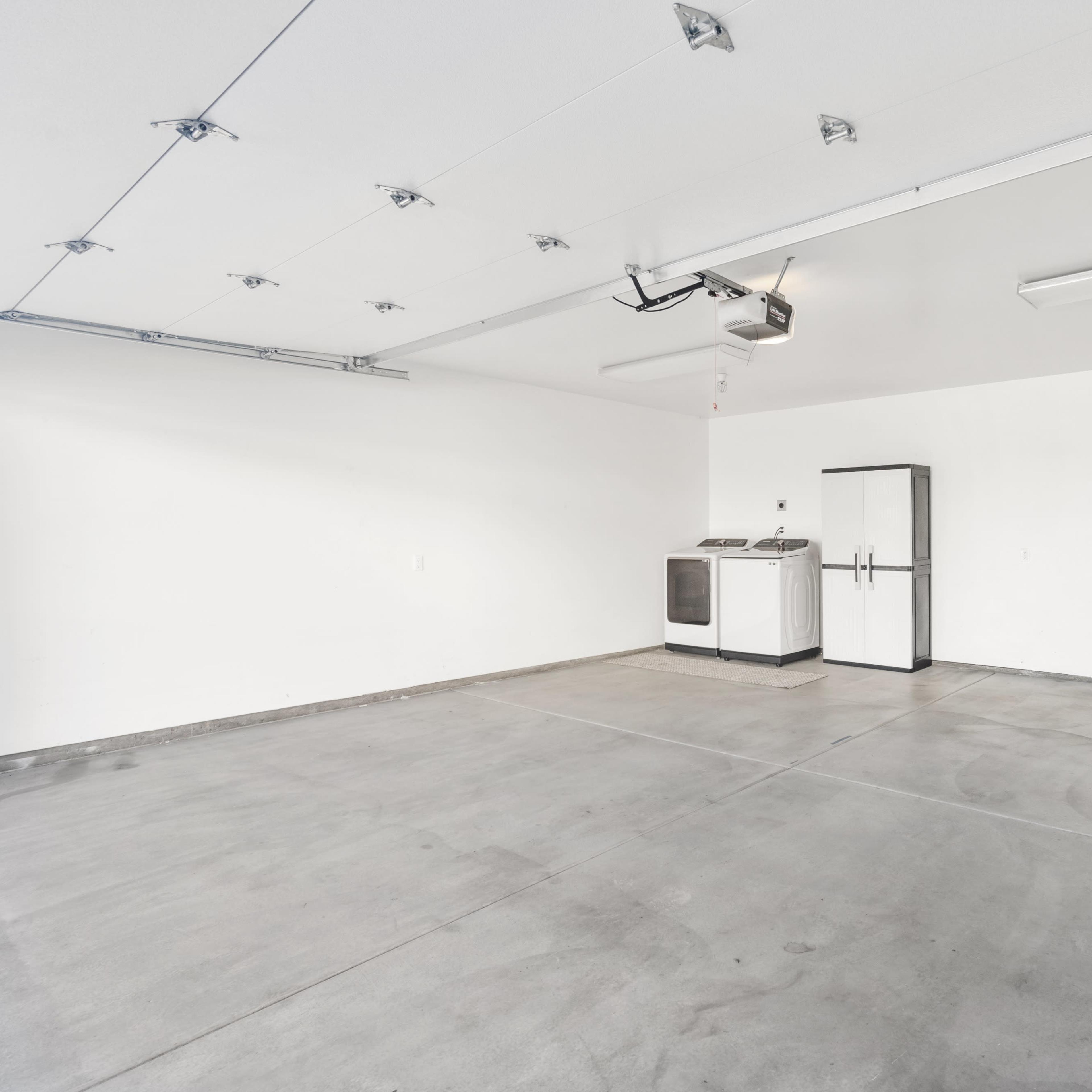 An empty garage featuring a washing machine, a refrigerator, and a door, all set against white walls and a concrete floor.