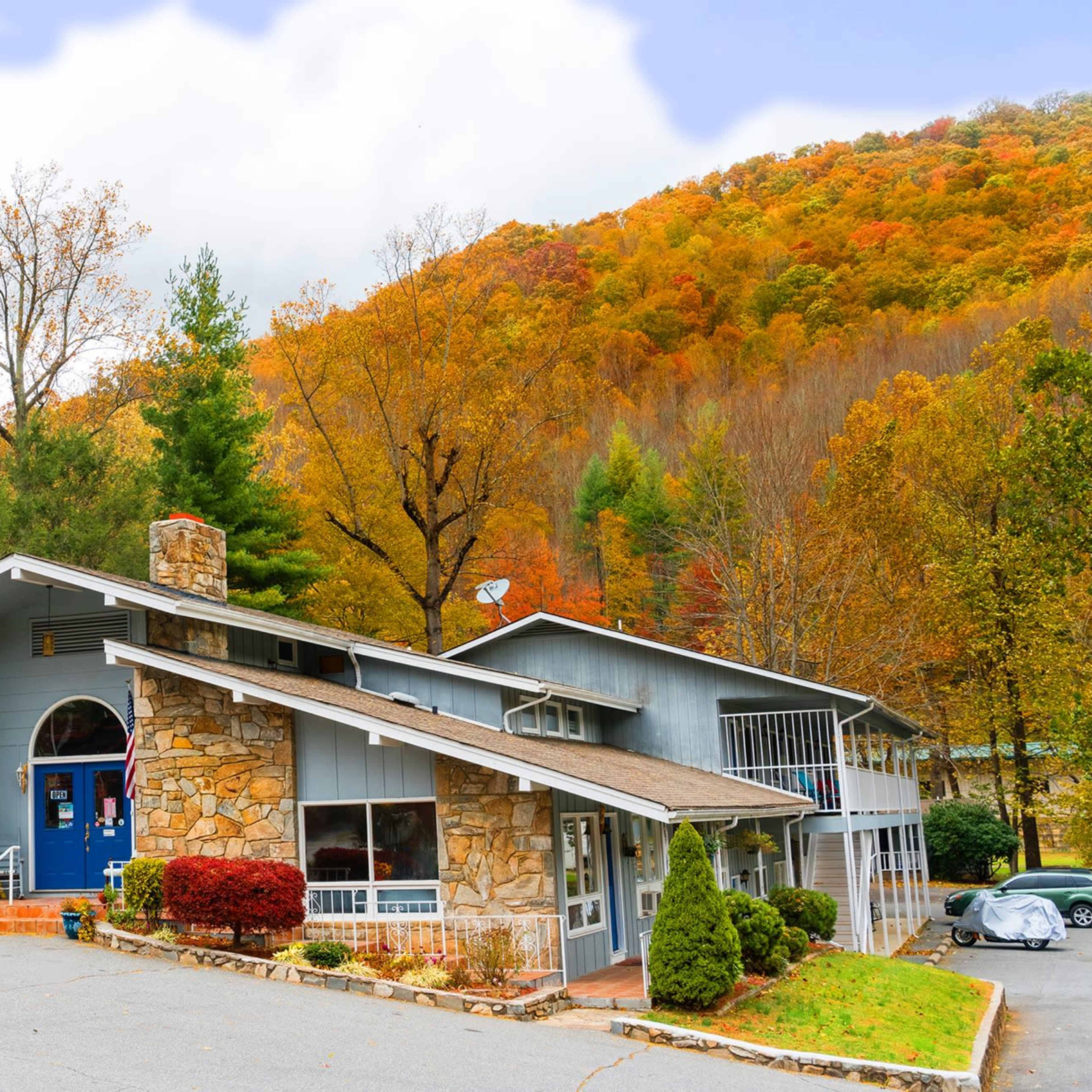 A modern building with stone and wood exterior sits at the base of a hillside adorned with autumn foliage.