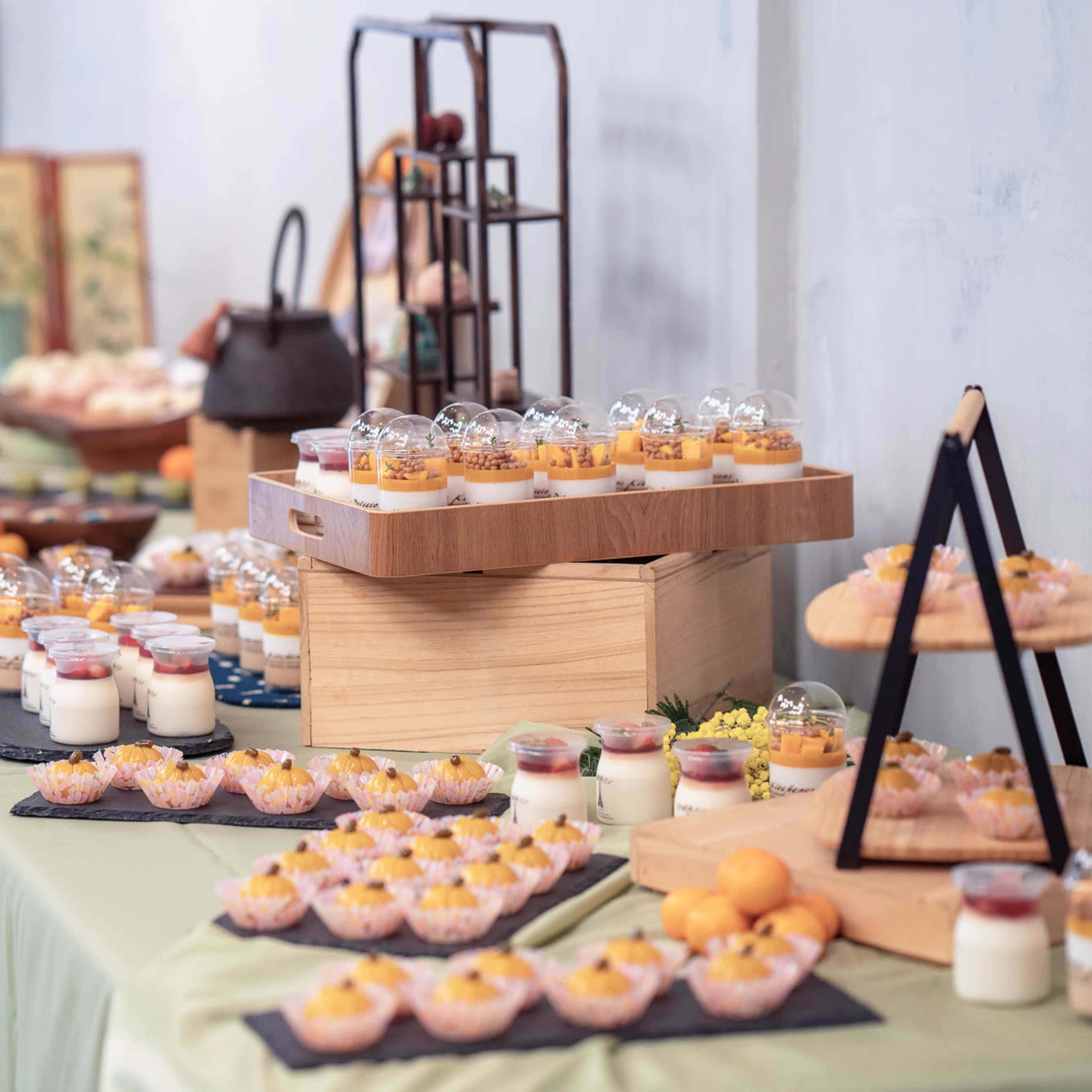 A decorative table is set with an array of desserts displayed on platters, jars, and cups.