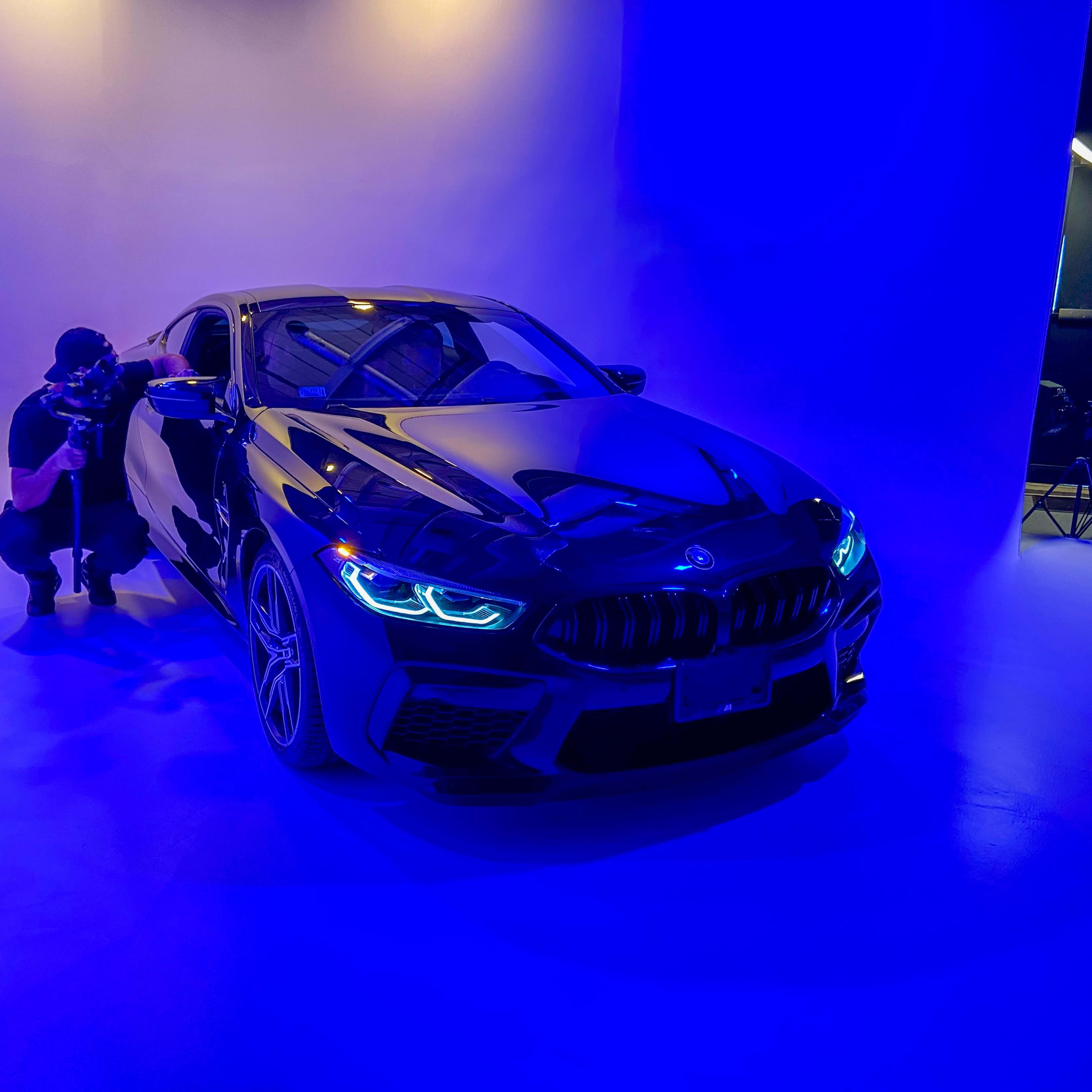 A photographer captures images of a black BMW car illuminated by blue lighting in a studio setting.